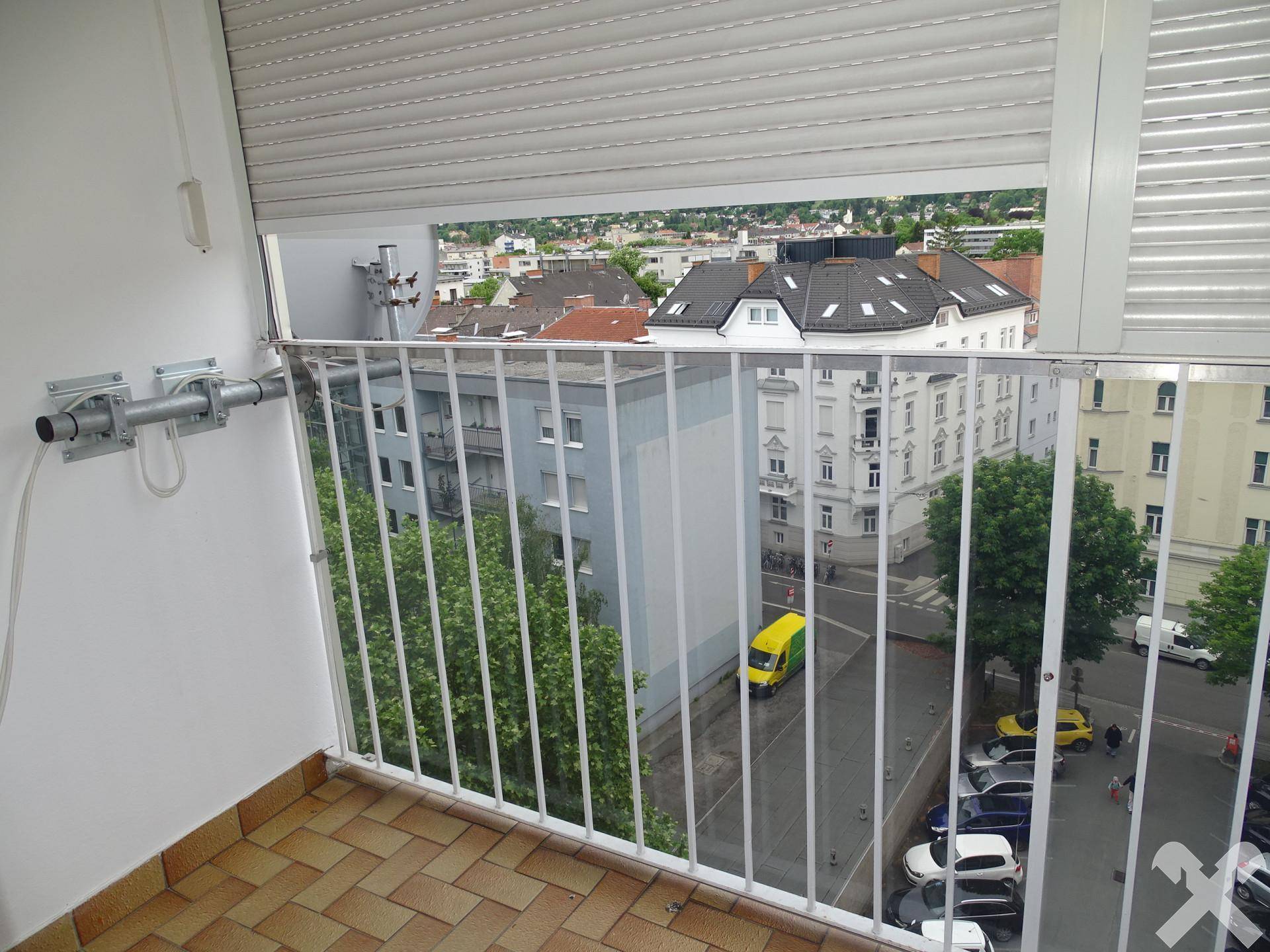 Balkon mit Fliesenboden und Rollladen, bietet einen Blick auf die Stadt.