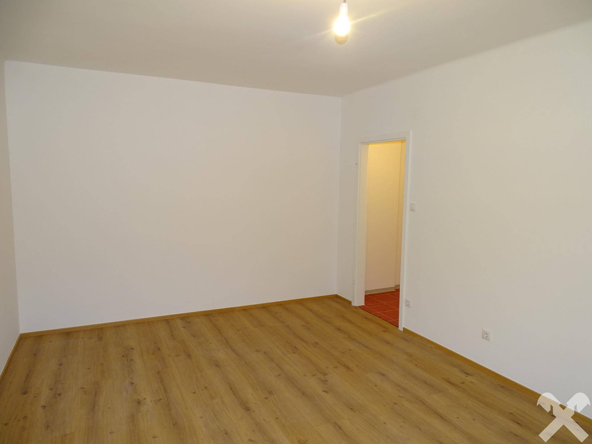 Helles Zimmer mit Laminatboden und Zugang zu einem weiteren Raum.