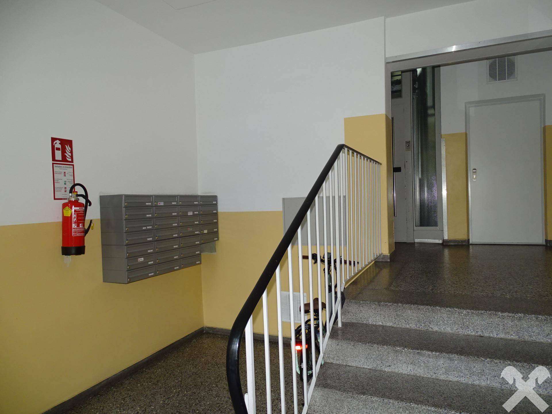 Eingangsbereich des Gebäudes mit Treppe, Briefkästen und Feuerlöscher.