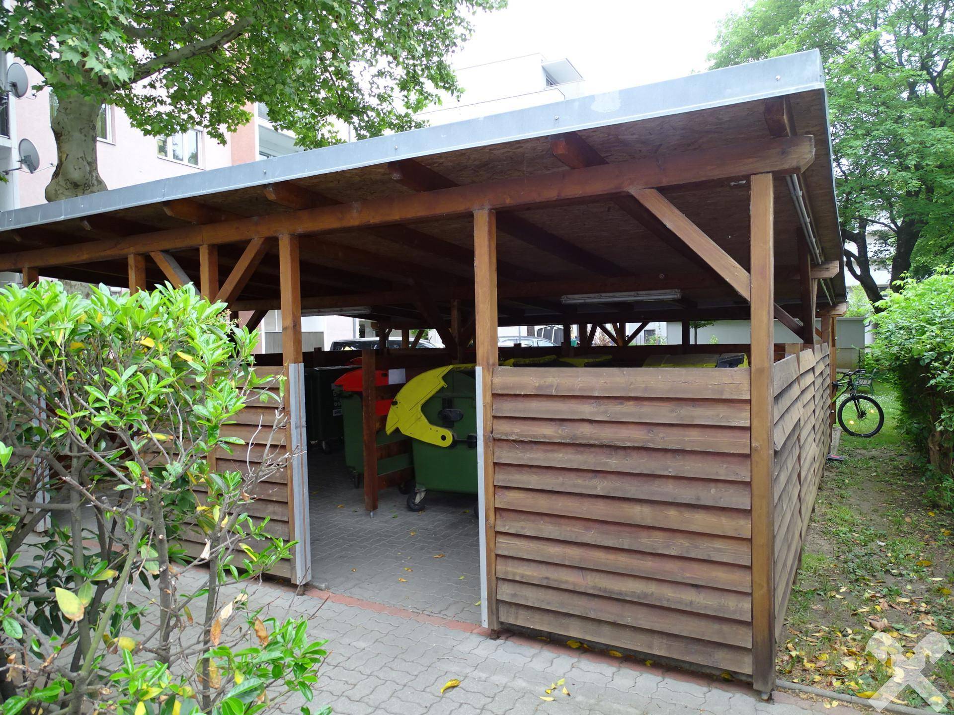 Überdachter Bereich für Mülltonnen im Außenbereich des Gebäudes.