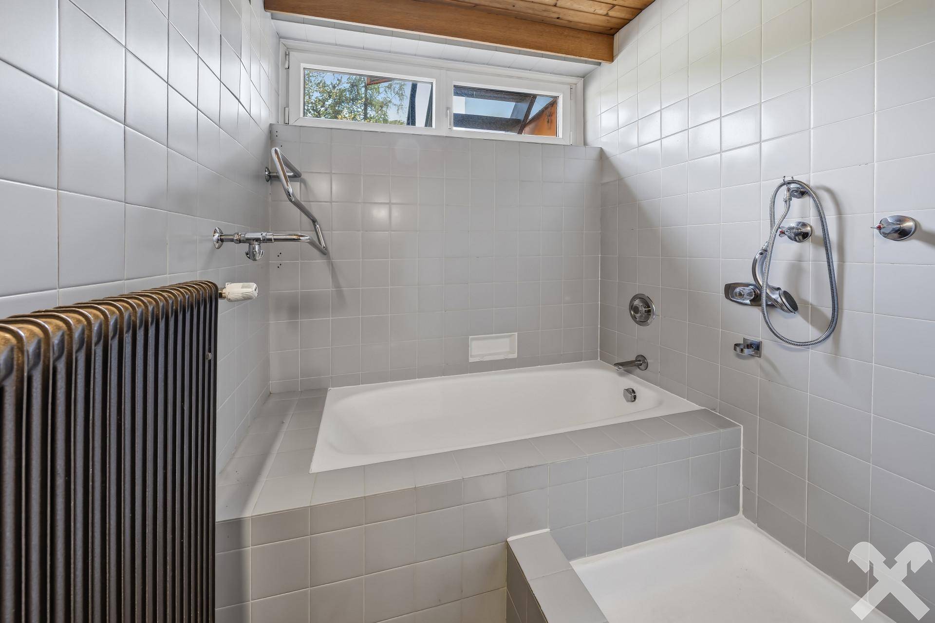 Badezimmer mit eingebauter Badewanne und grauen Fliesen.