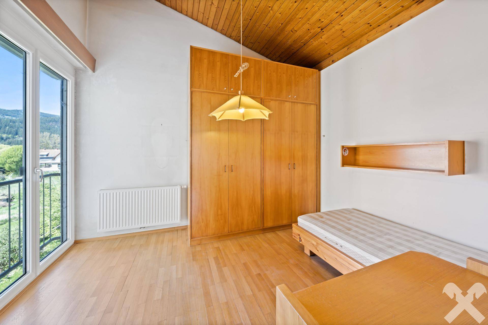 Helles Schlafzimmer mit Holzboden, Einbauschränken und Balkonzugang.