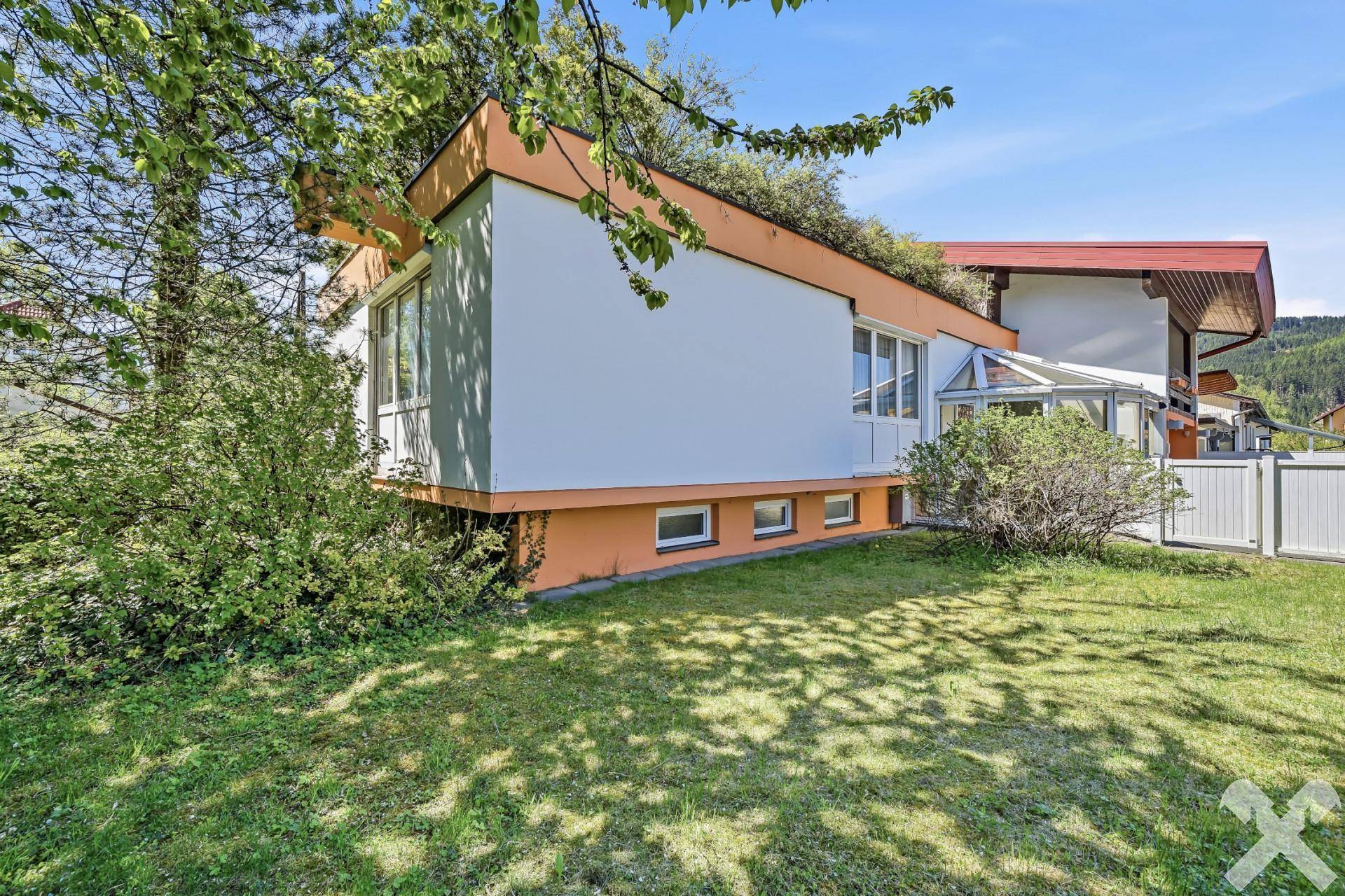 Seitenansicht des Hauses mit gepflegtem Rasen, üppiger Bepflanzung und einem Wintergarten.