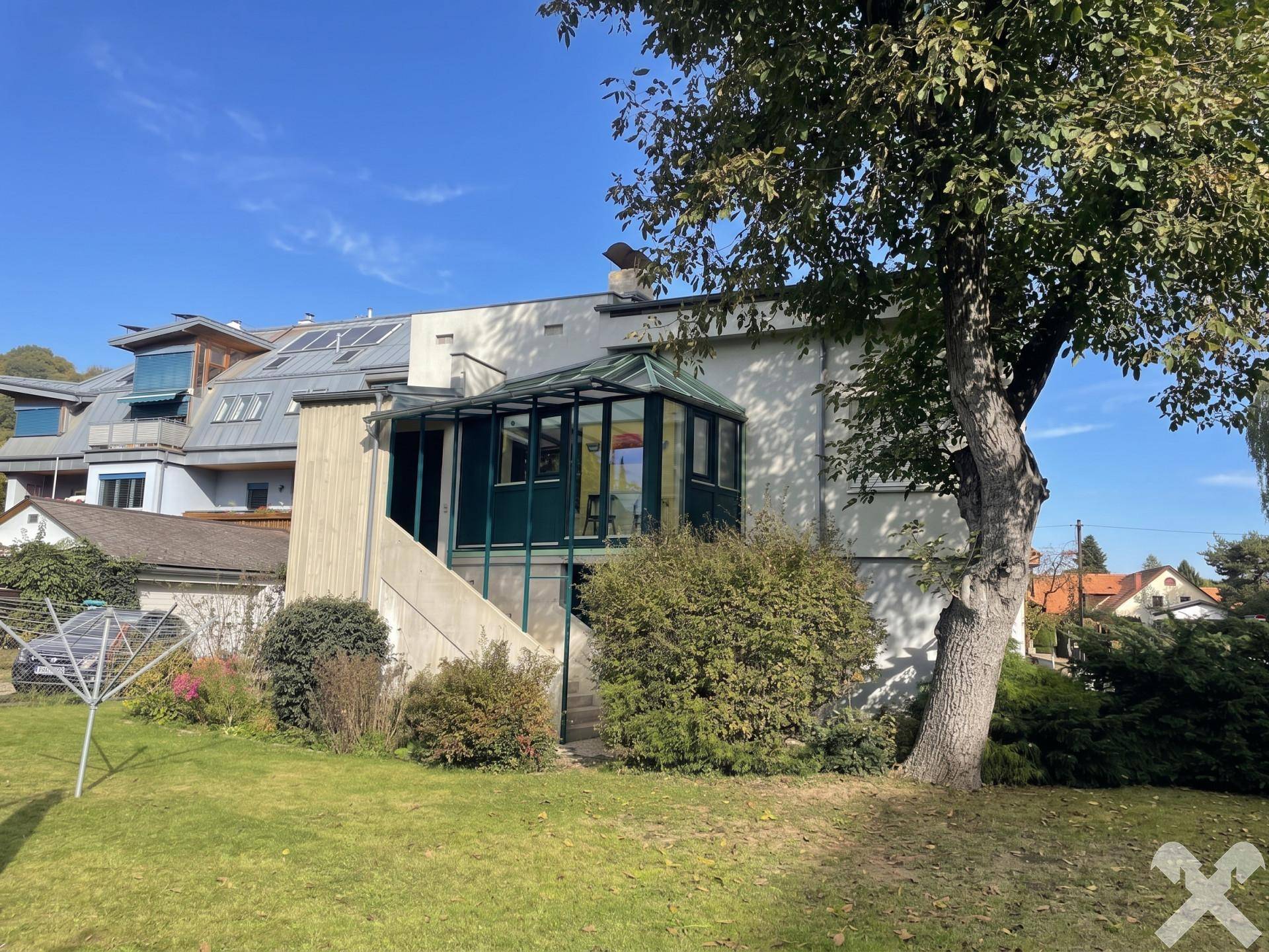 Ansicht des Hauses von hinten mit Wintergarten und großem Garten unter blauem Himmel.
