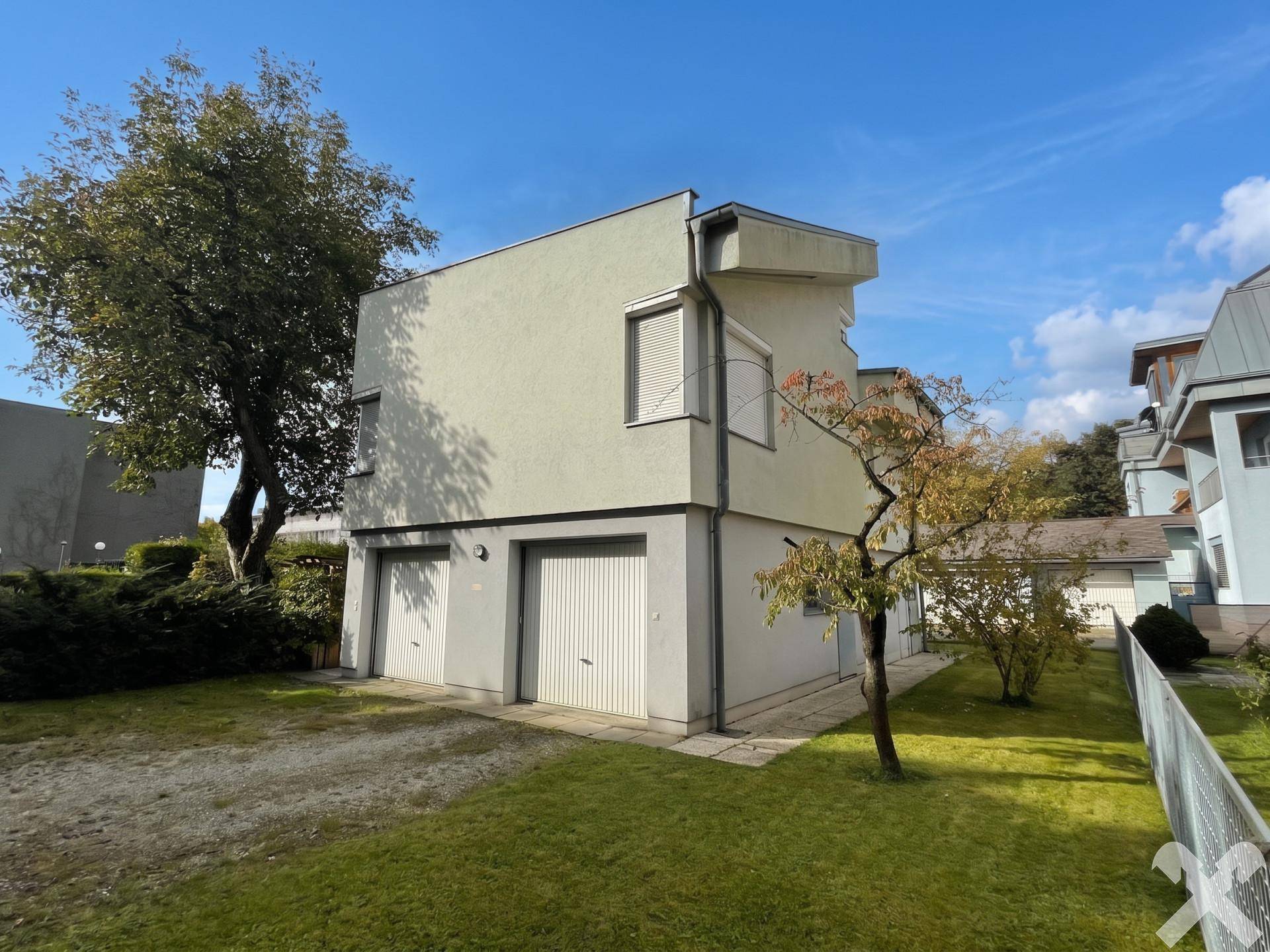 Seitliche Ansicht des Hauses mit zwei Garagentoren und gepflegtem Rasenbereich.