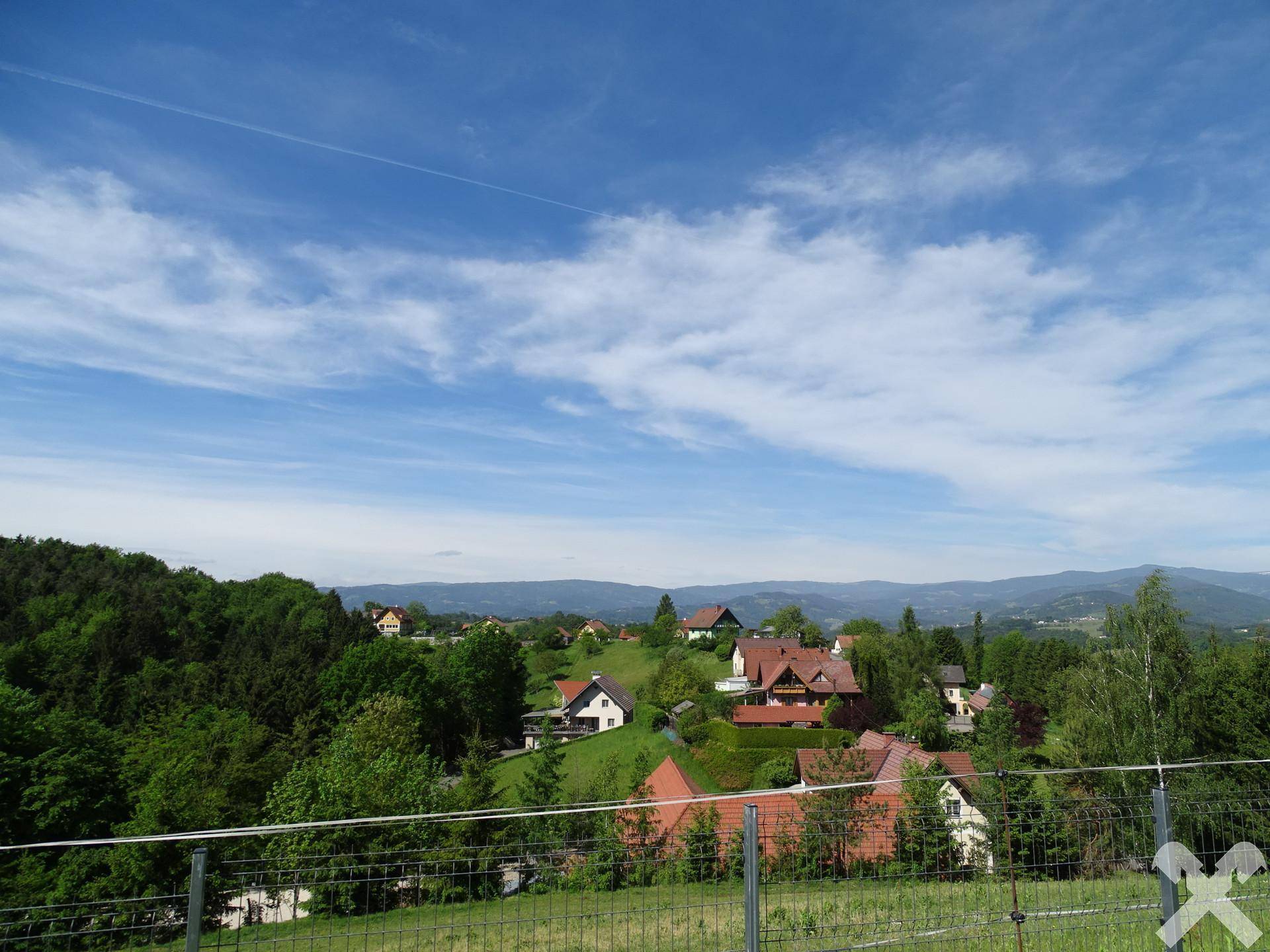 Weitläufiger Blick über die grüne Landschaft mit verstreuten Häusern und Bergen im Hintergrund.