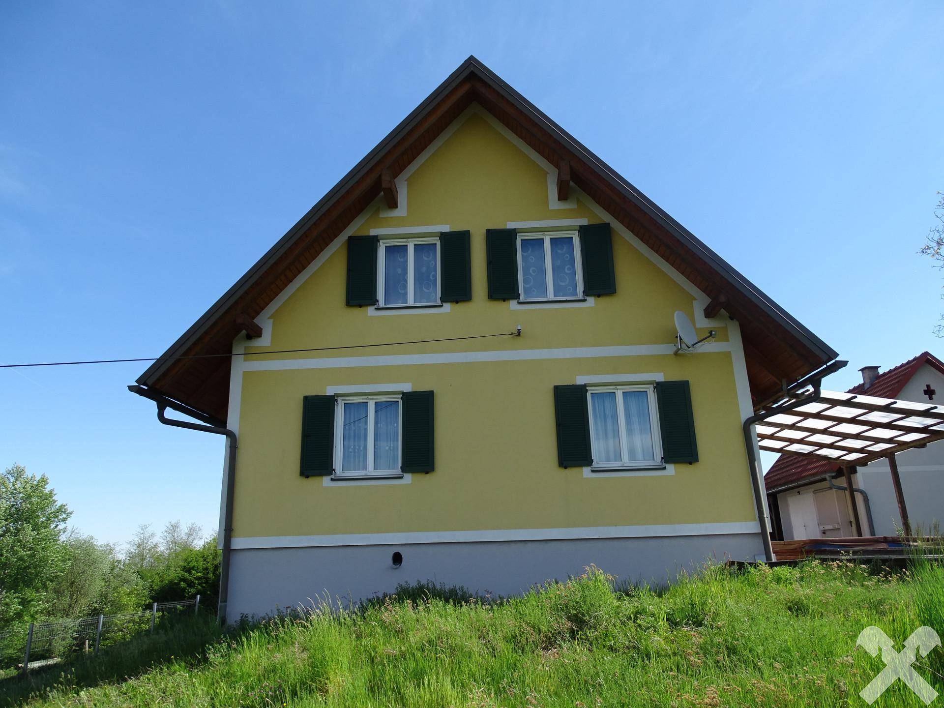Vorderansicht des gelben Hauses mit Satteldach und grünen Fensterläden.