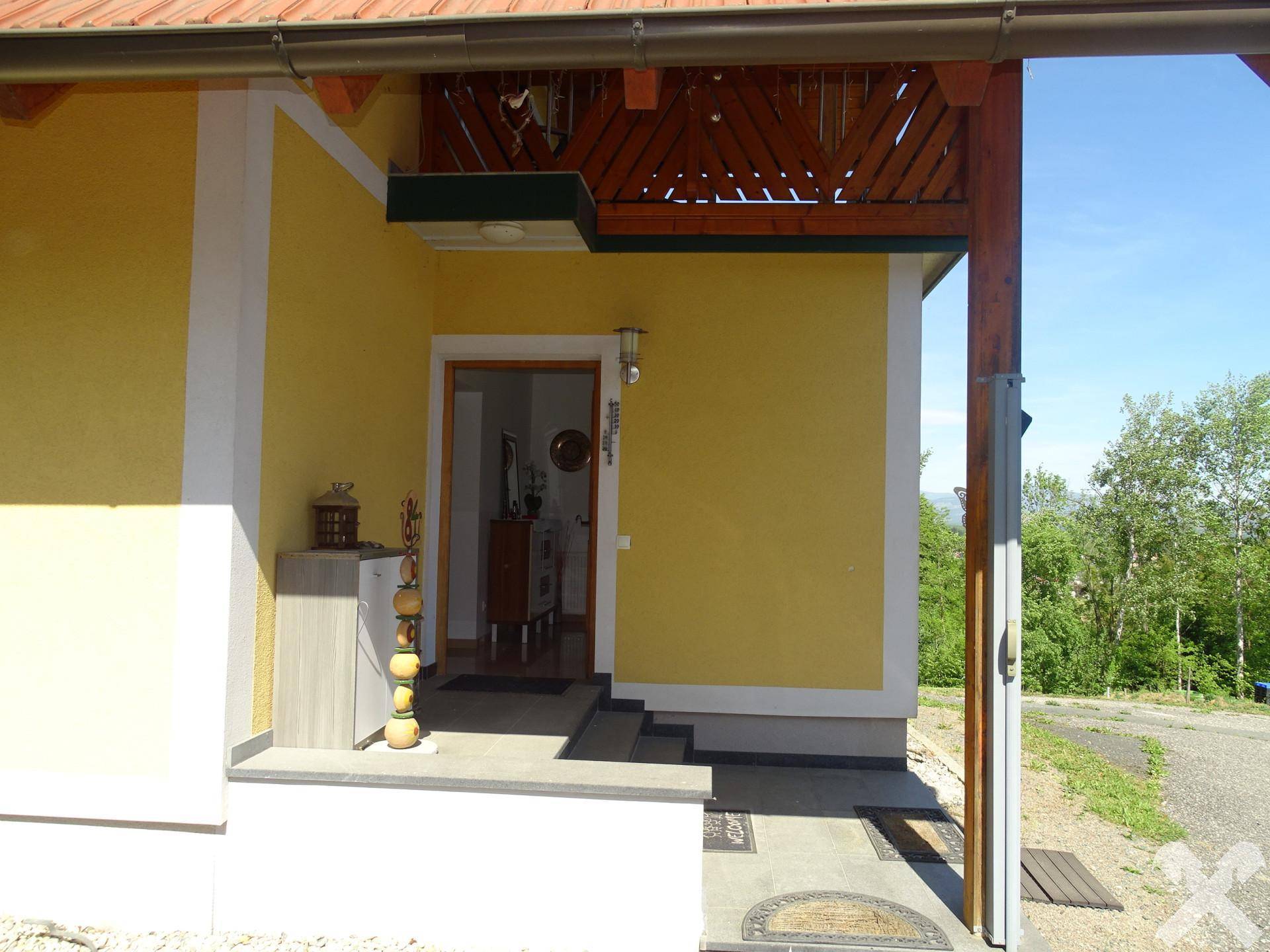 Eingangsbereich des Hauses mit gelber Fassade und Holzbalkon darüber.