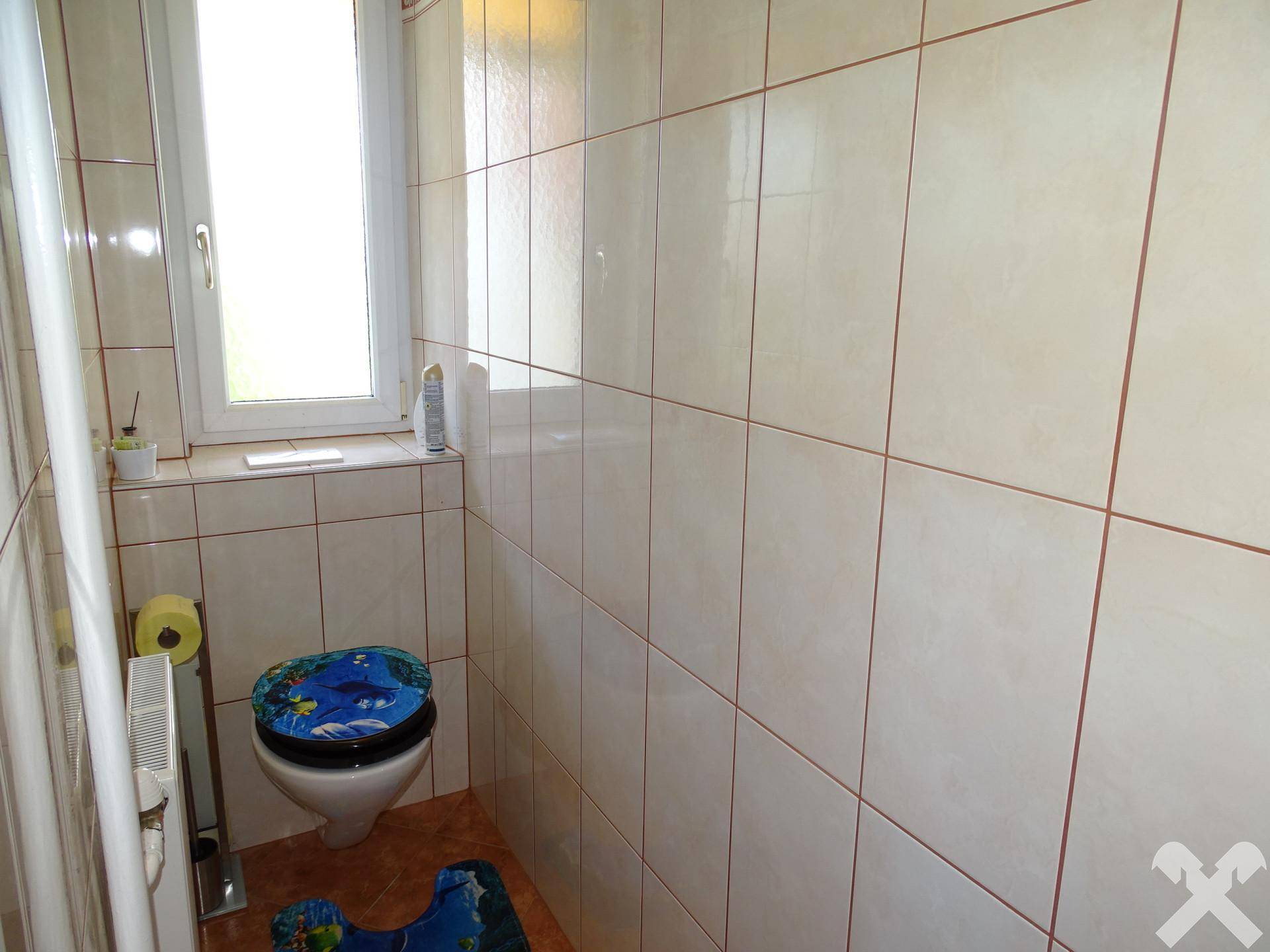 Kleines WC mit beigefarbenen Fliesen, Fenster und Heizkörper.