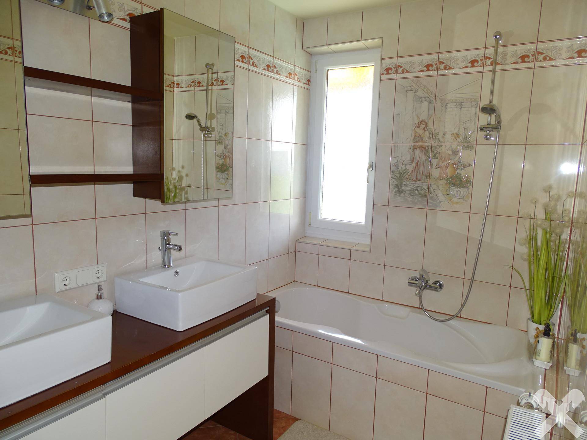 Badezimmer mit Badewanne, Doppelwaschbecken und beigefarbenen Fliesen.