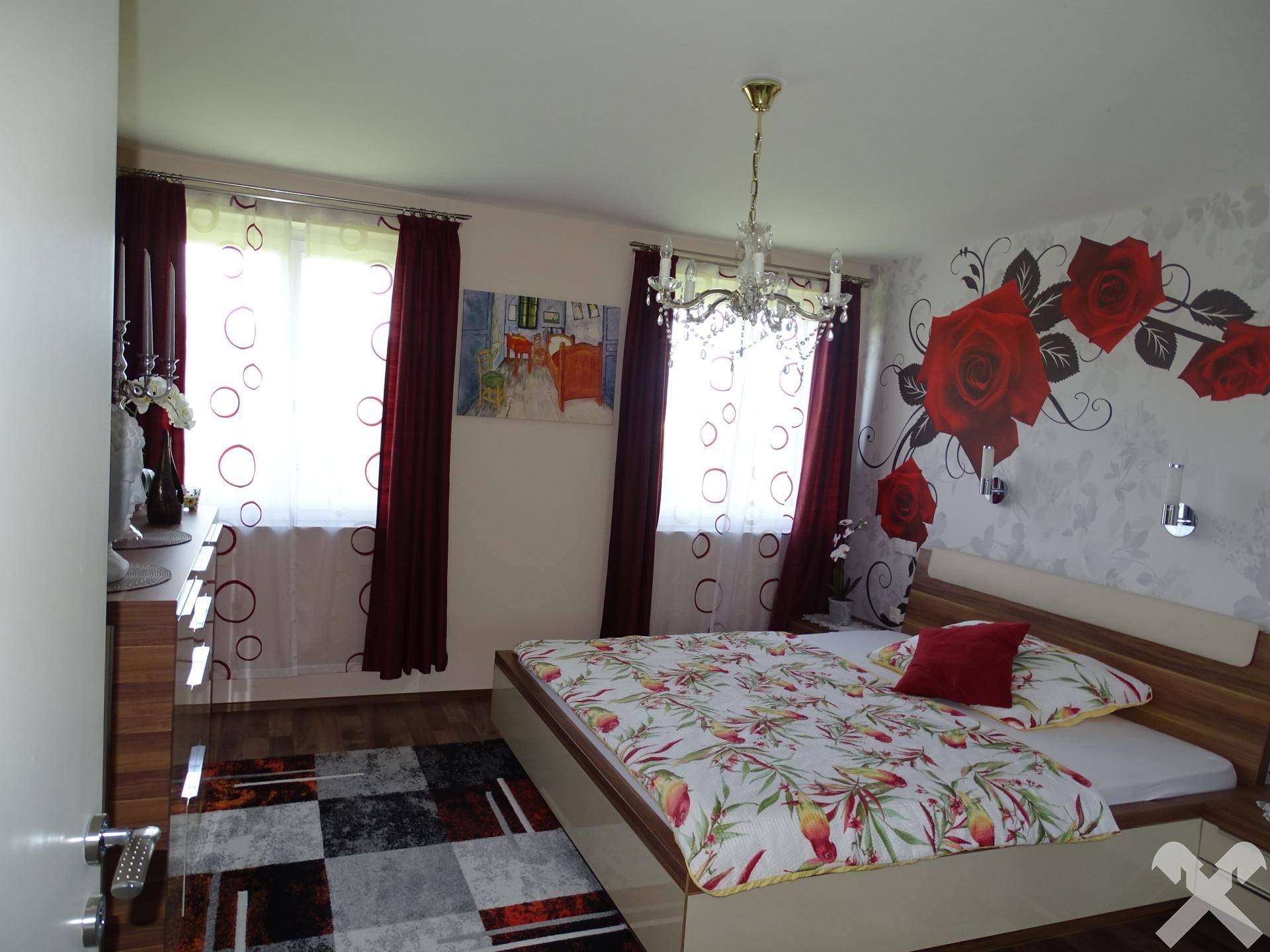 Schlafzimmer mit Doppelbett, floraler Wanddekoration und Kronleuchter.