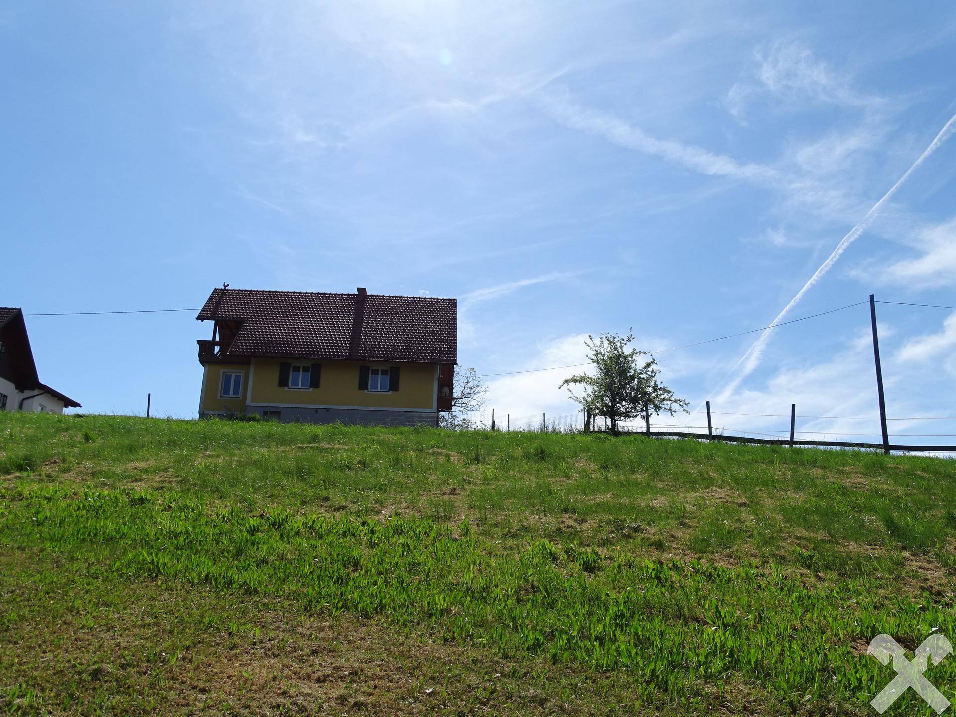 Gelbes Haus mit rotem Dach auf einem grünen Hügel unter blauem Himmel.