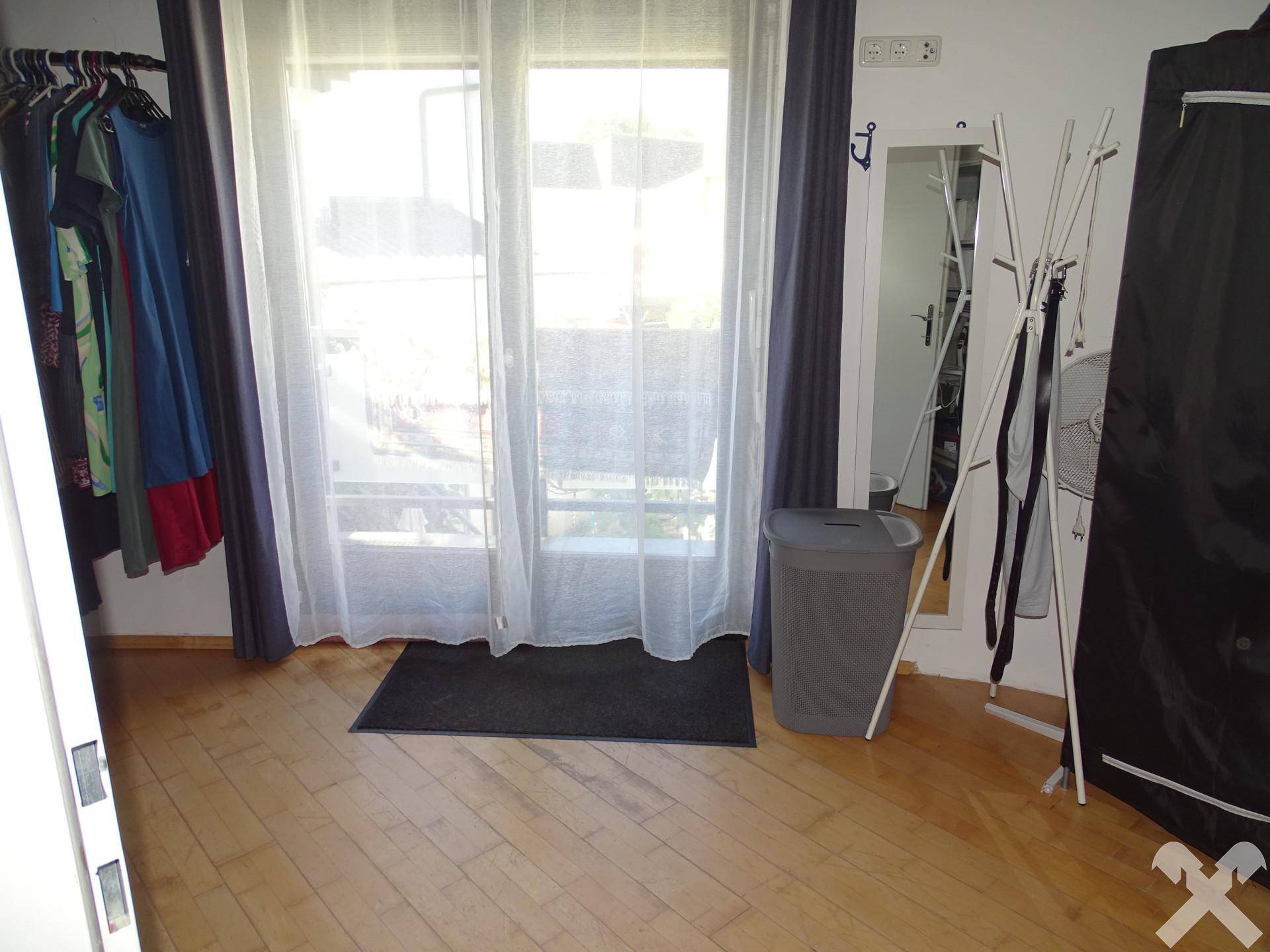 Heller Raum mit Holzboden, großem Fenster und Platz für Kleideraufbewahrung.
