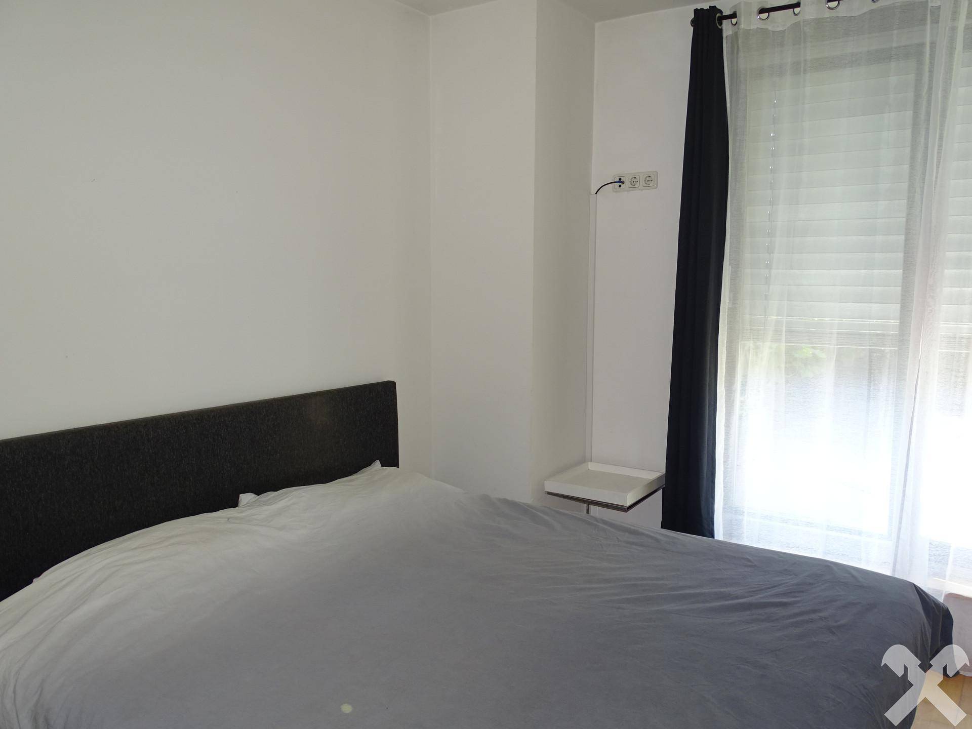 Schlafzimmer mit Doppelbett, hellen Wänden und großem Fenster mit Vorhängen.