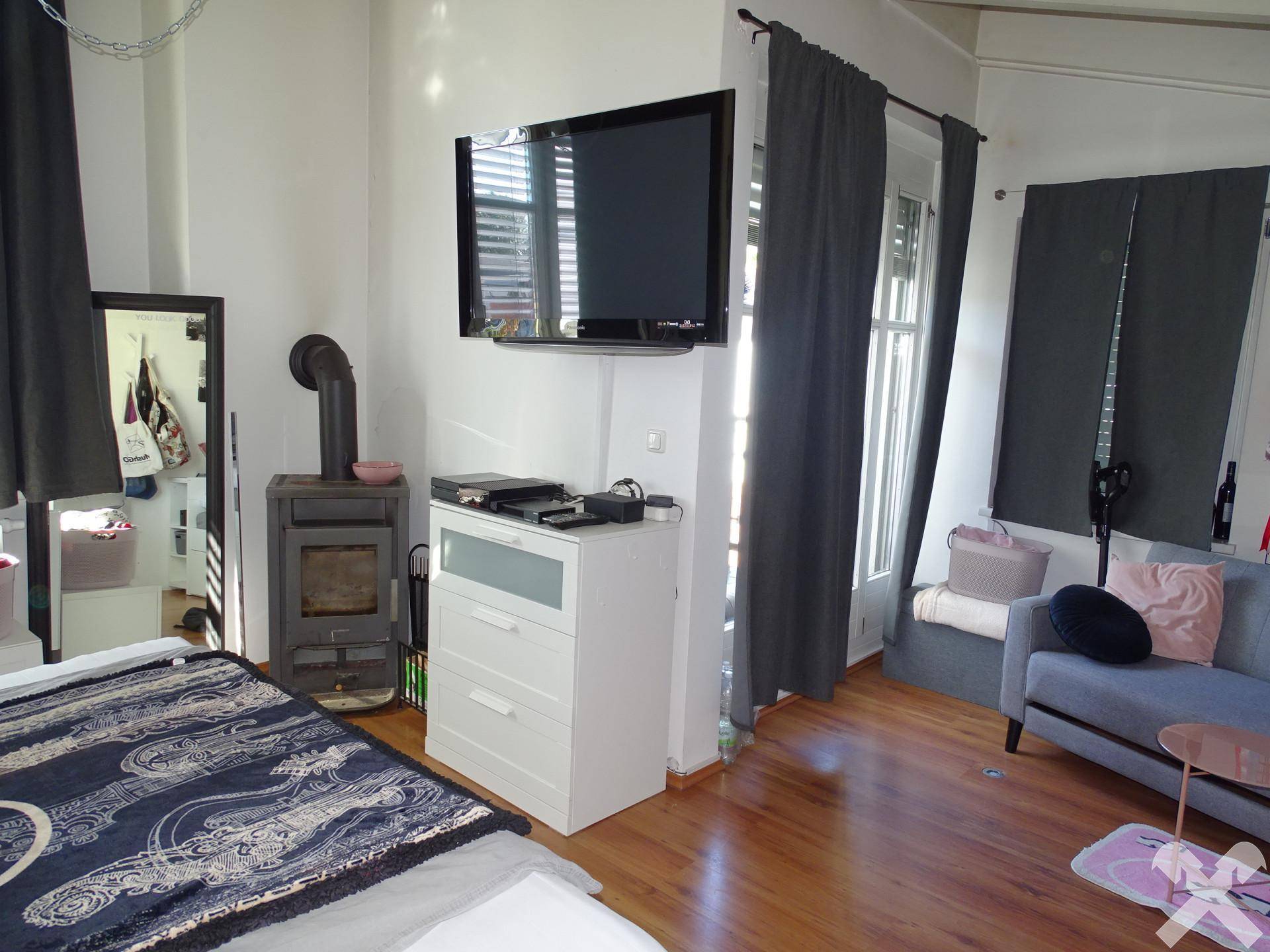Gemütliches Schlafzimmer mit Holzboden, Kaminofen und Zugang zu einem Balkon.