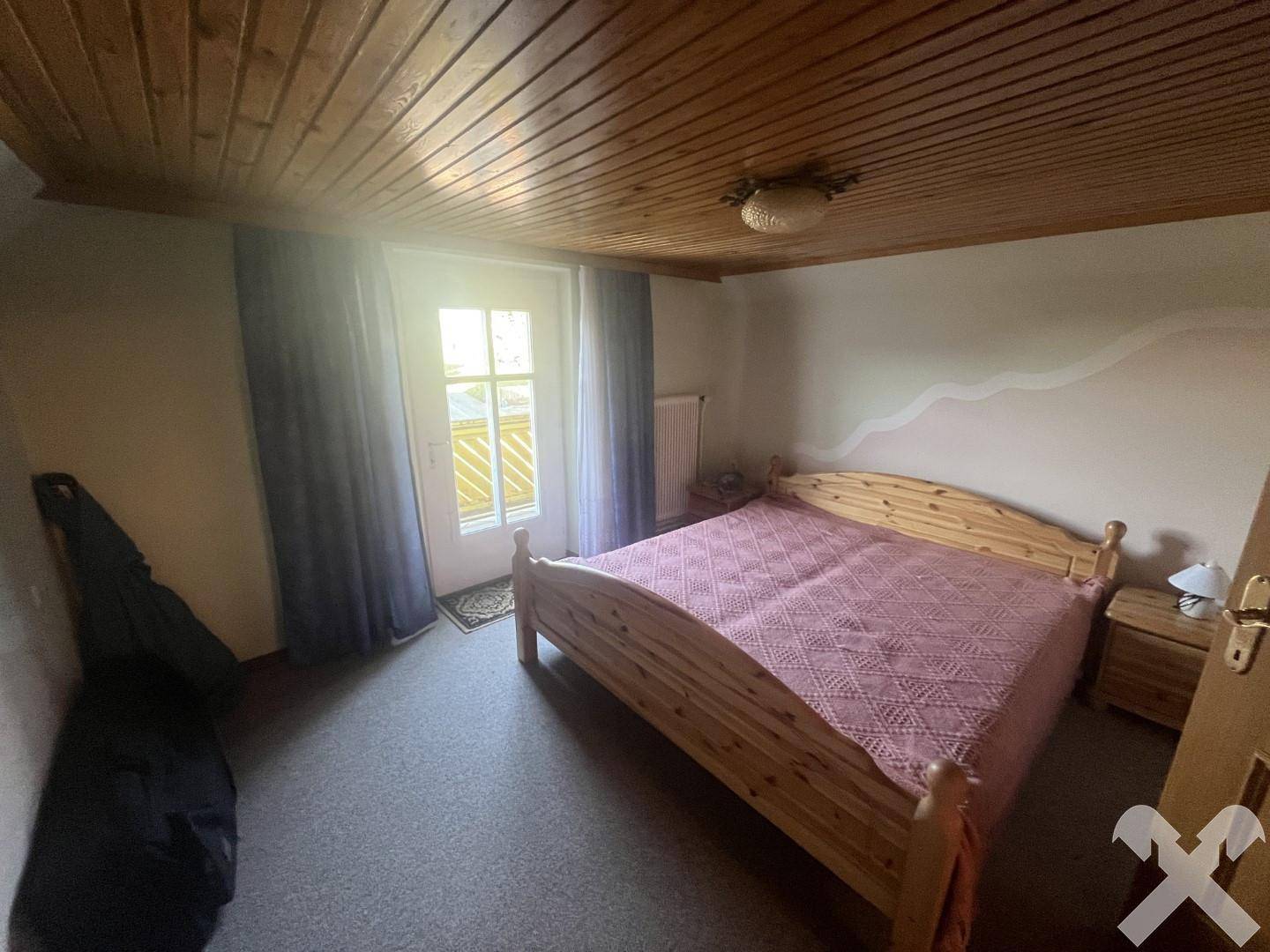 Schlafzimmer mit Holzdoppelbett, Holzdecke und einer Tür, die Zugang zu einem Balkon bietet.