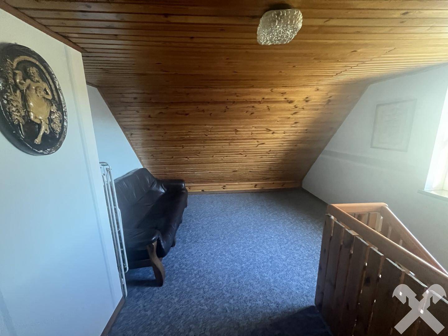 Dachbodenbereich mit schräger Holzdecke und blauem Teppichboden, der zusätzlichen Stauraum bietet.