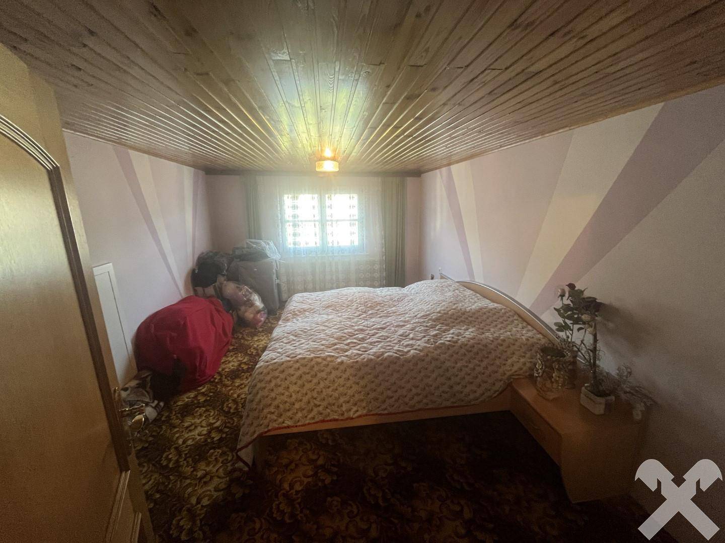 Schlafzimmer mit Doppelbett, Holzdecke und einem Fenster, das den Raum mit Licht durchflutet.