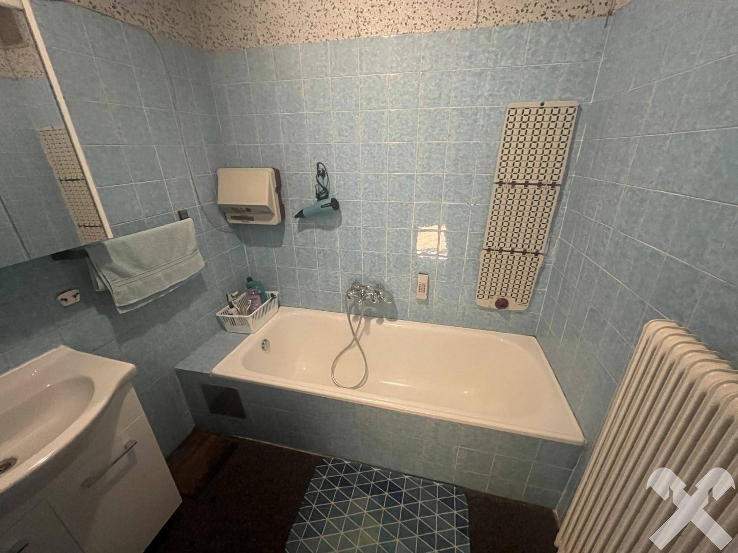 Badezimmer mit blauen Fliesen, Badewanne und Heizkörper, im Stil der 80er Jahre gehalten.