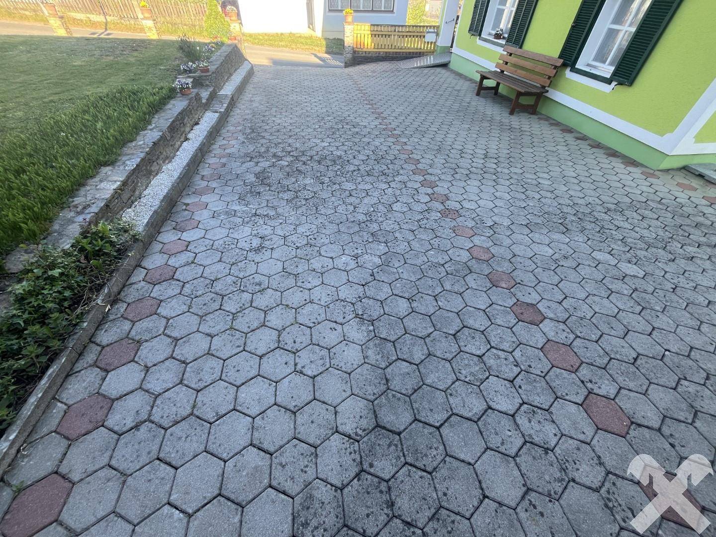 Gepflasterter Weg mit sechseckigen grauen und roten Fliesen, der zum Eingang des Hauses führt.