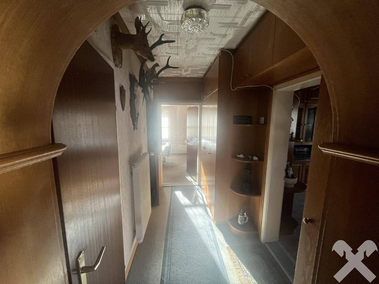 Langer Flur mit Holzschränken und traditionellen Hirschgeweihen an der Wand, der zu weiteren Räumen führt.