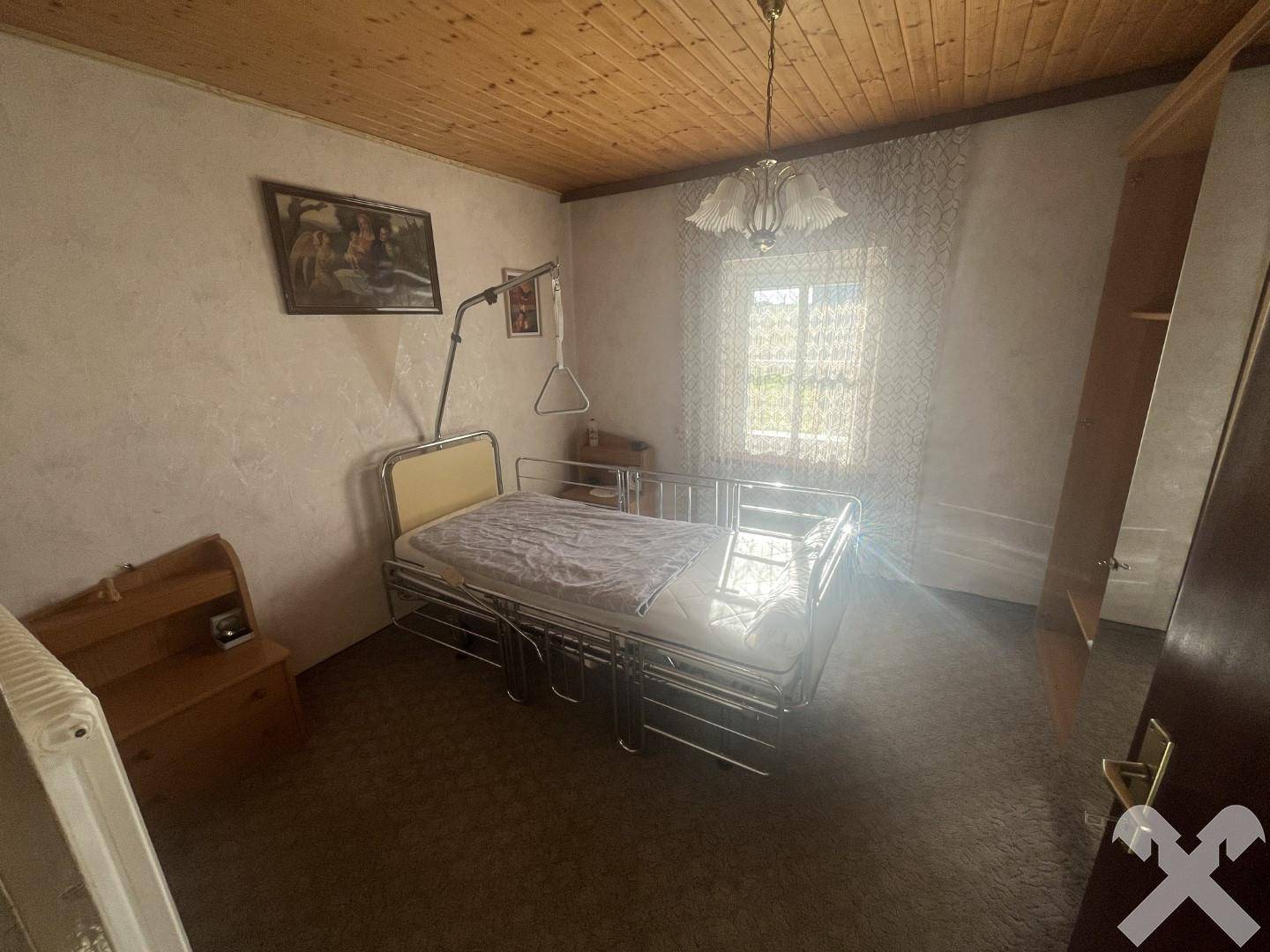 Schlafzimmer mit Einzelbett, Holzdecke und einem Fenster, das den Raum mit Tageslicht erhellt.