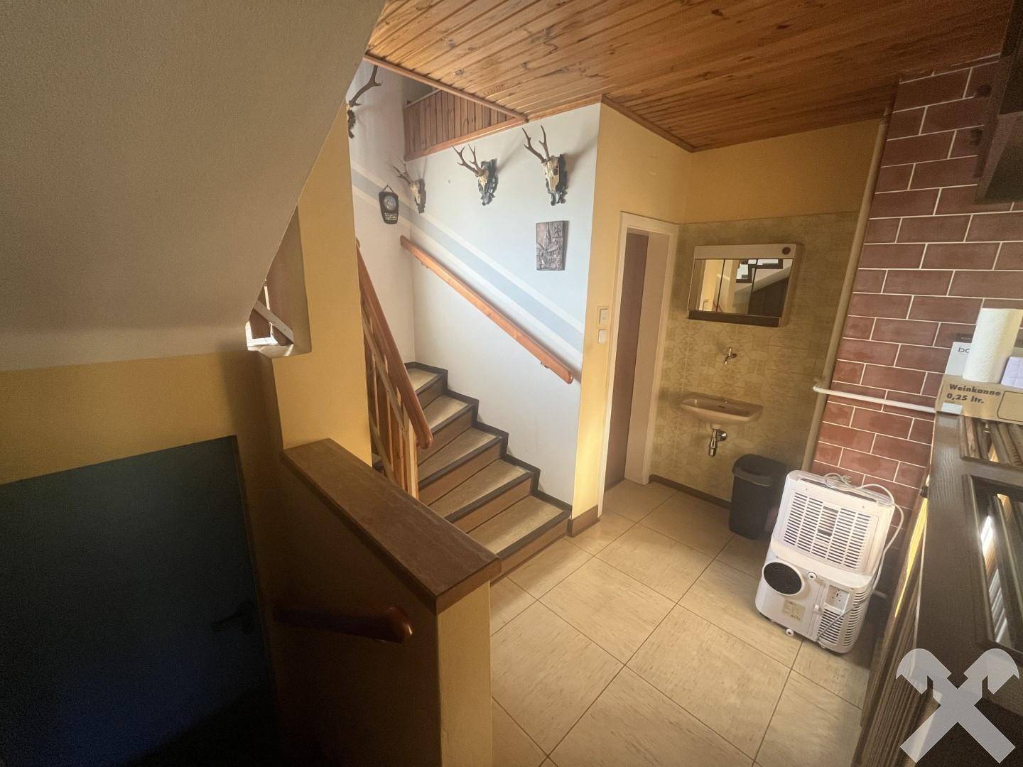 Treppenhaus mit Fliesenboden, Holztreppe und traditionellen Hirschgeweihen als Wanddekoration.