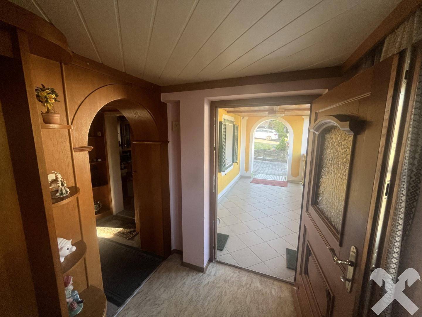 Heller Flur mit Holzvertäfelung und Blick auf den überdachten Eingangsbereich mit Fliesenboden.