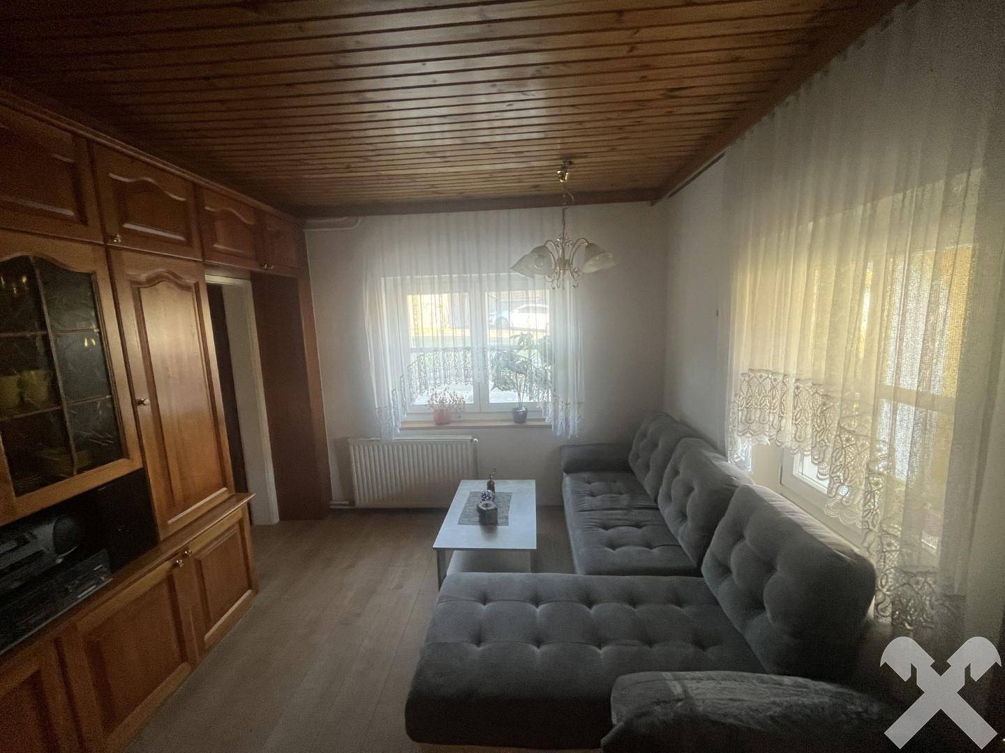 Wohnzimmer mit gemütlichem grauen Sofa, Holzdecke und traditionellen Holzmöbeln, die eine warme Atmosphäre schaffen.