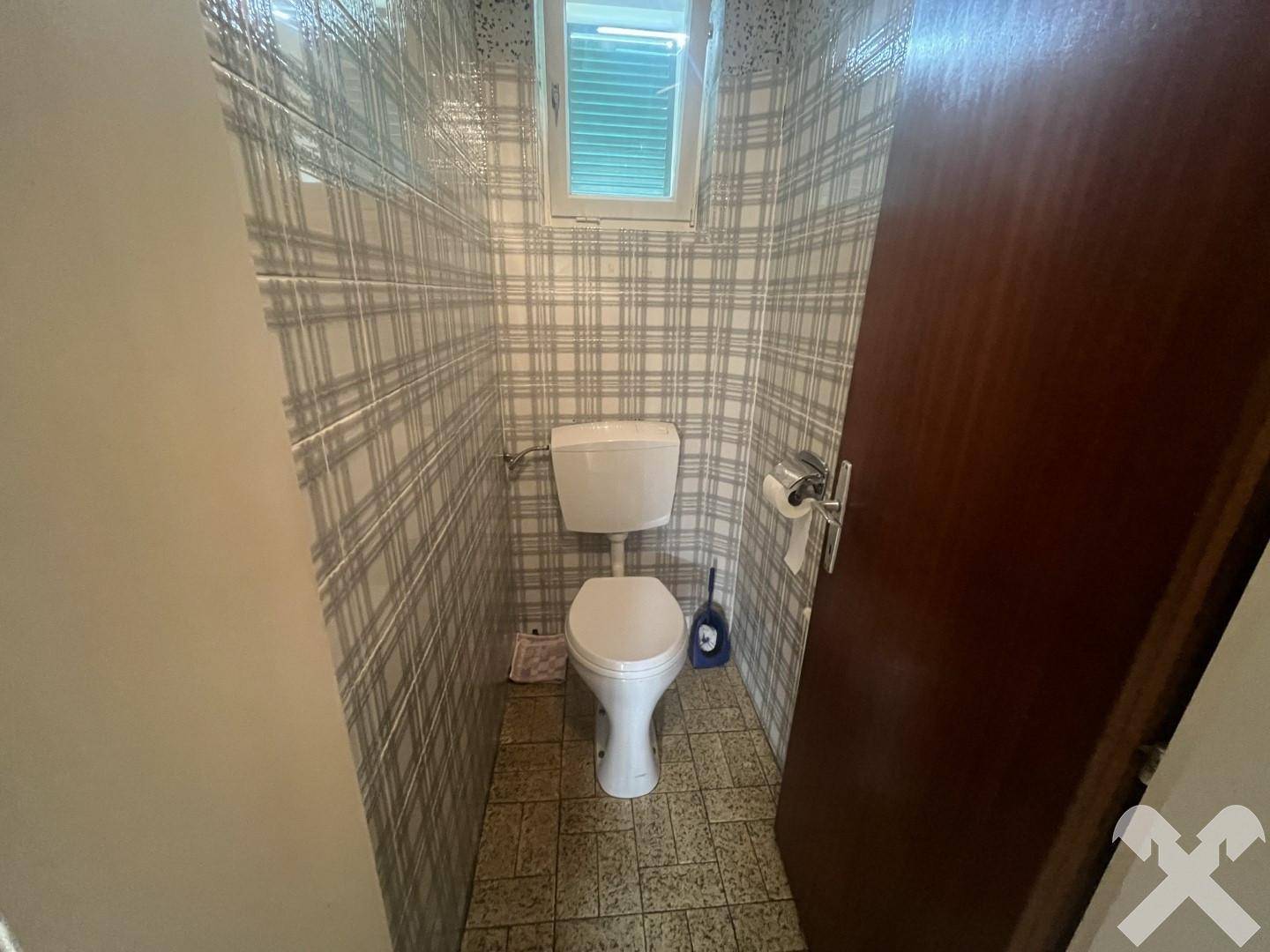 Kleines WC mit karierten Fliesen, Toilette und Fenster für natürliche Belüftung des Raumes.