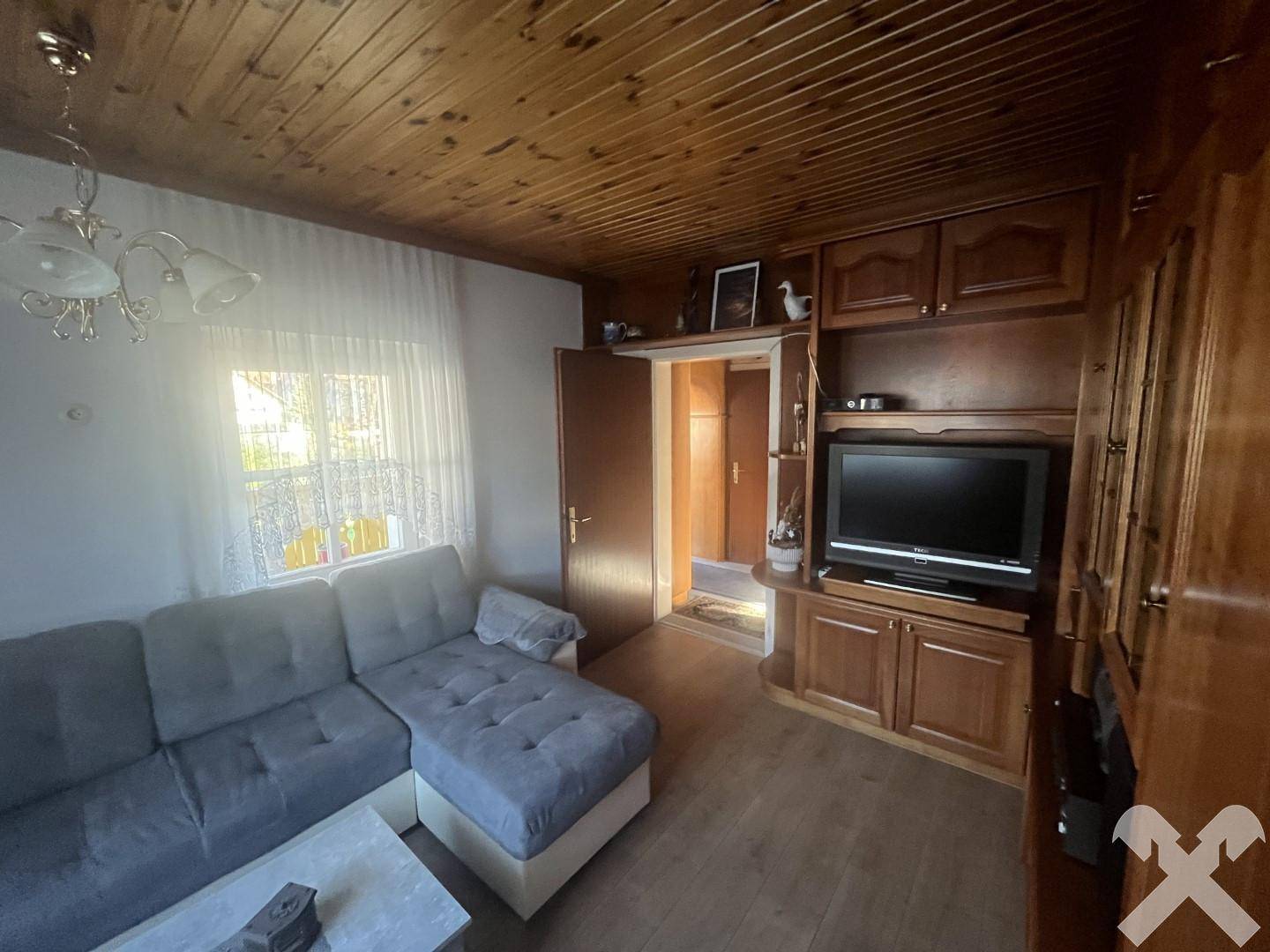 Wohnzimmer mit Holzdecke, traditionellen Möbeln und einem Fernseher, der in eine Schrankwand integriert ist.