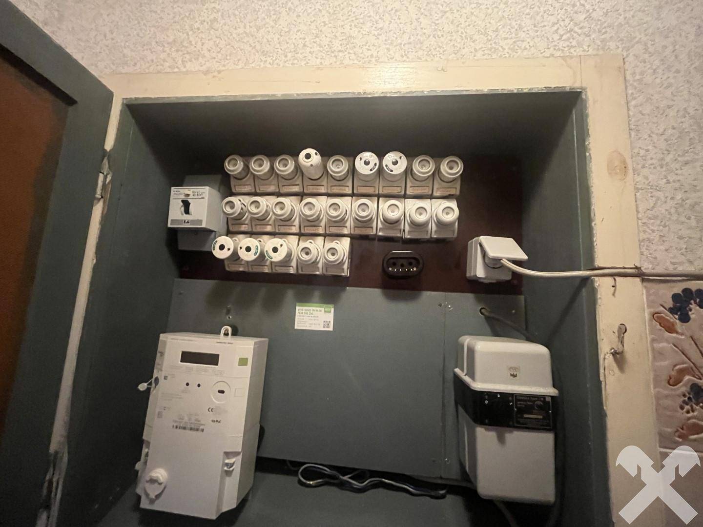 Elektrischer Sicherungskasten mit Zählern und vielen Sicherungen, in einem Funktionsraum untergebracht.