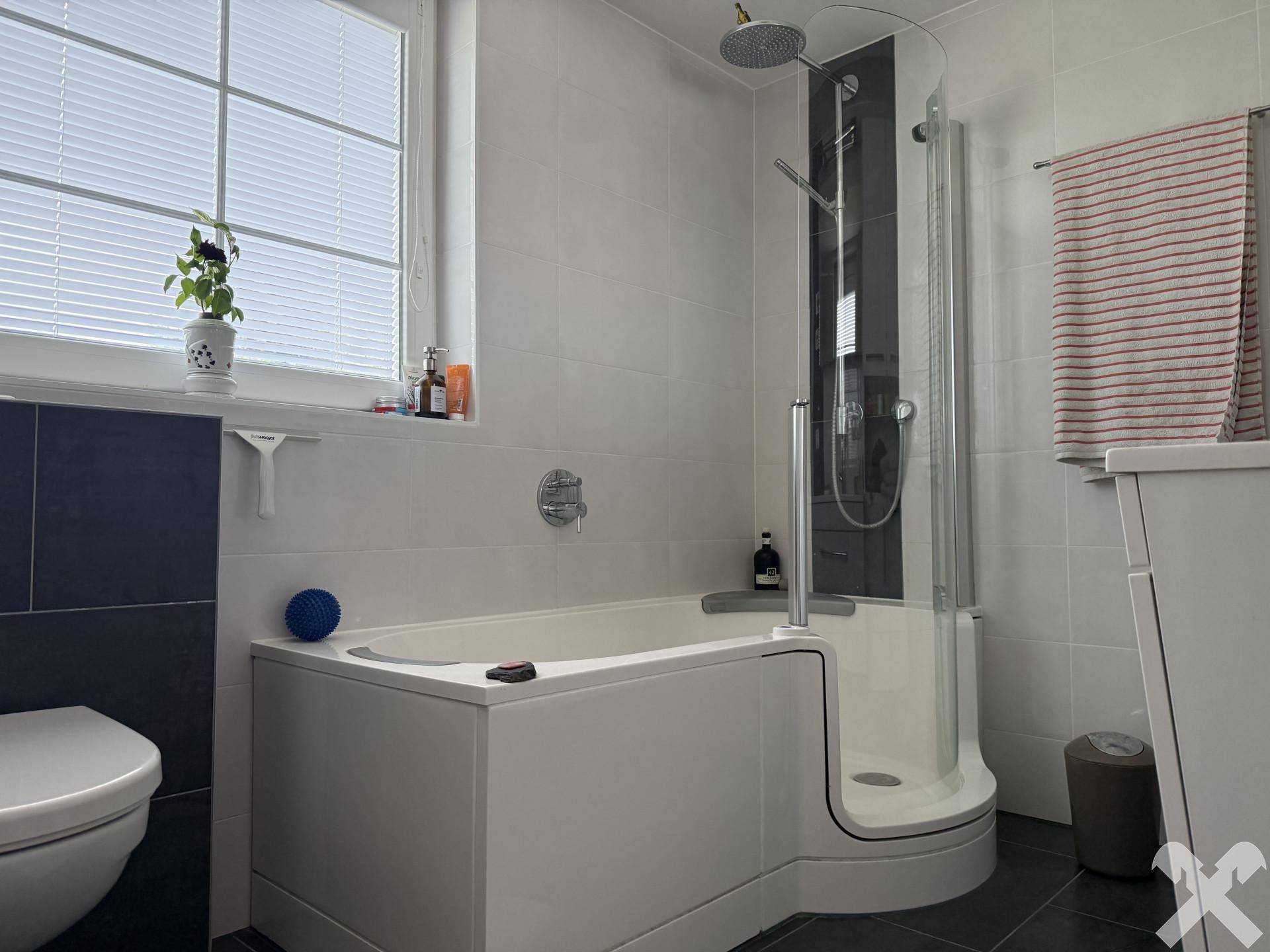 Modernes Badezimmer mit Badewanne, integrierter Dusche, Fliesen und einem Fenster für Tageslicht.