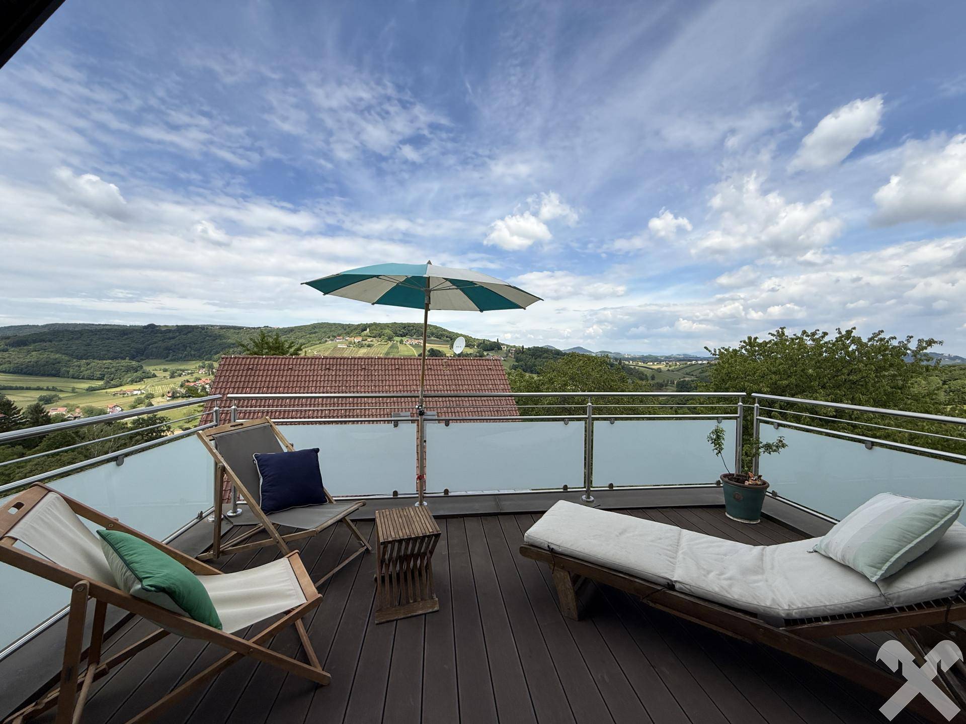 Große Sonnenterrasse mit Liegestühlen, Sonnenschirm und weitem Blick über die Landschaft.