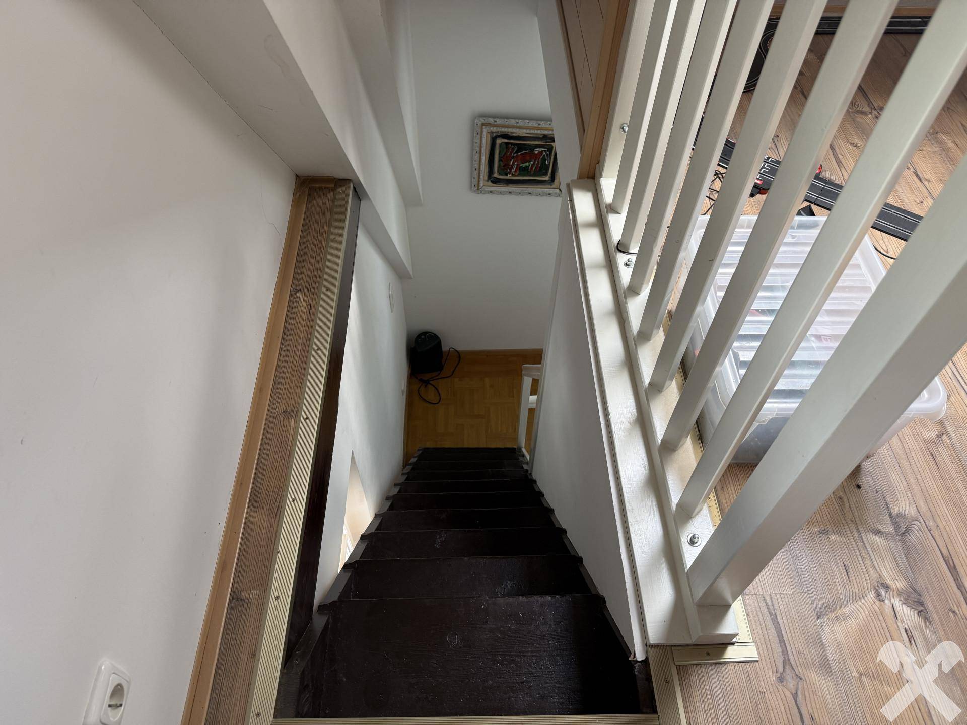 Blick von oben auf eine dunkle Holztreppe mit weißen Geländern, die nach unten führt.