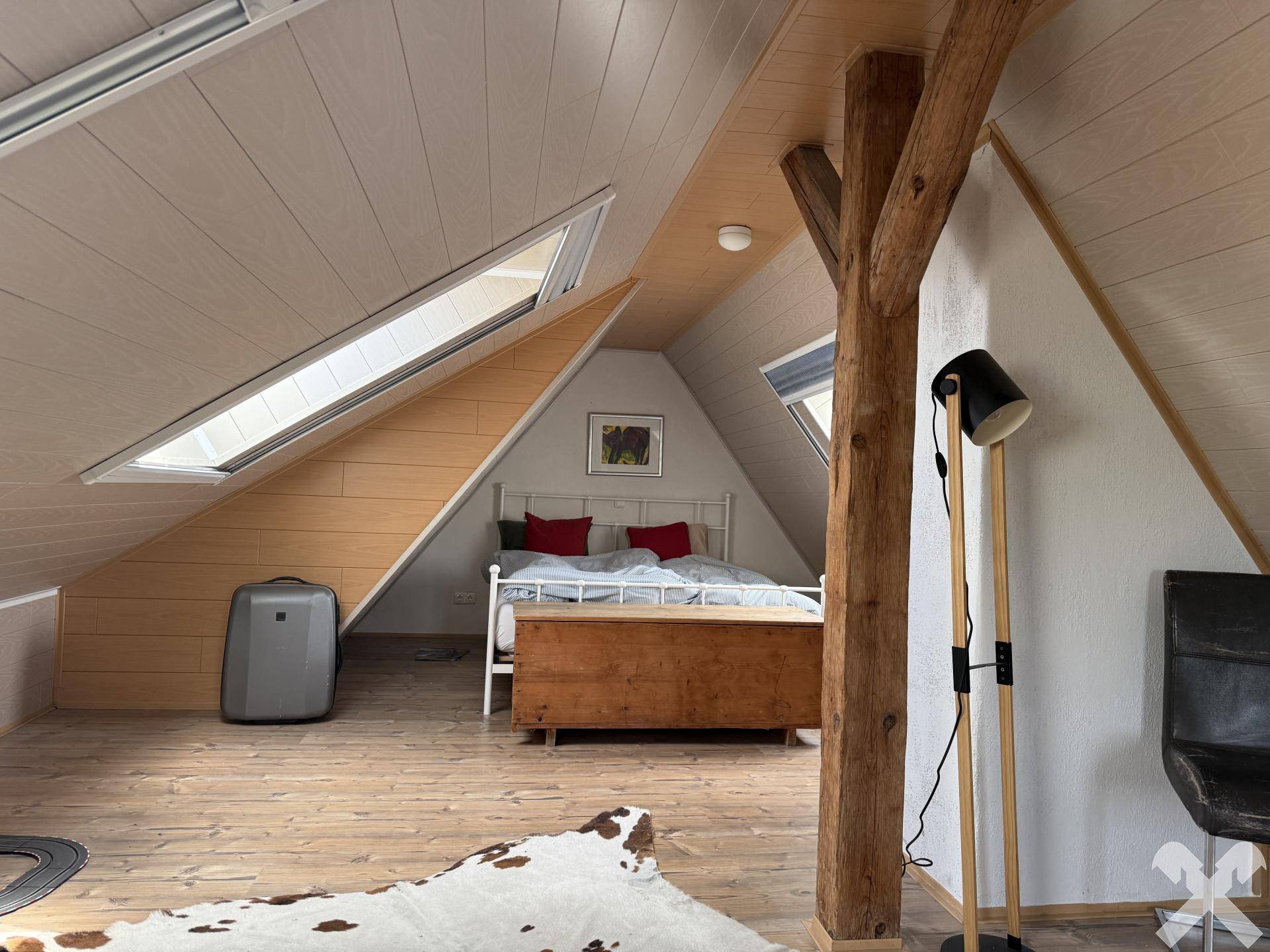 Gemütliches Schlafzimmer im Dachgeschoss mit Dachschrägen, Holzbalken und Dachfenstern.