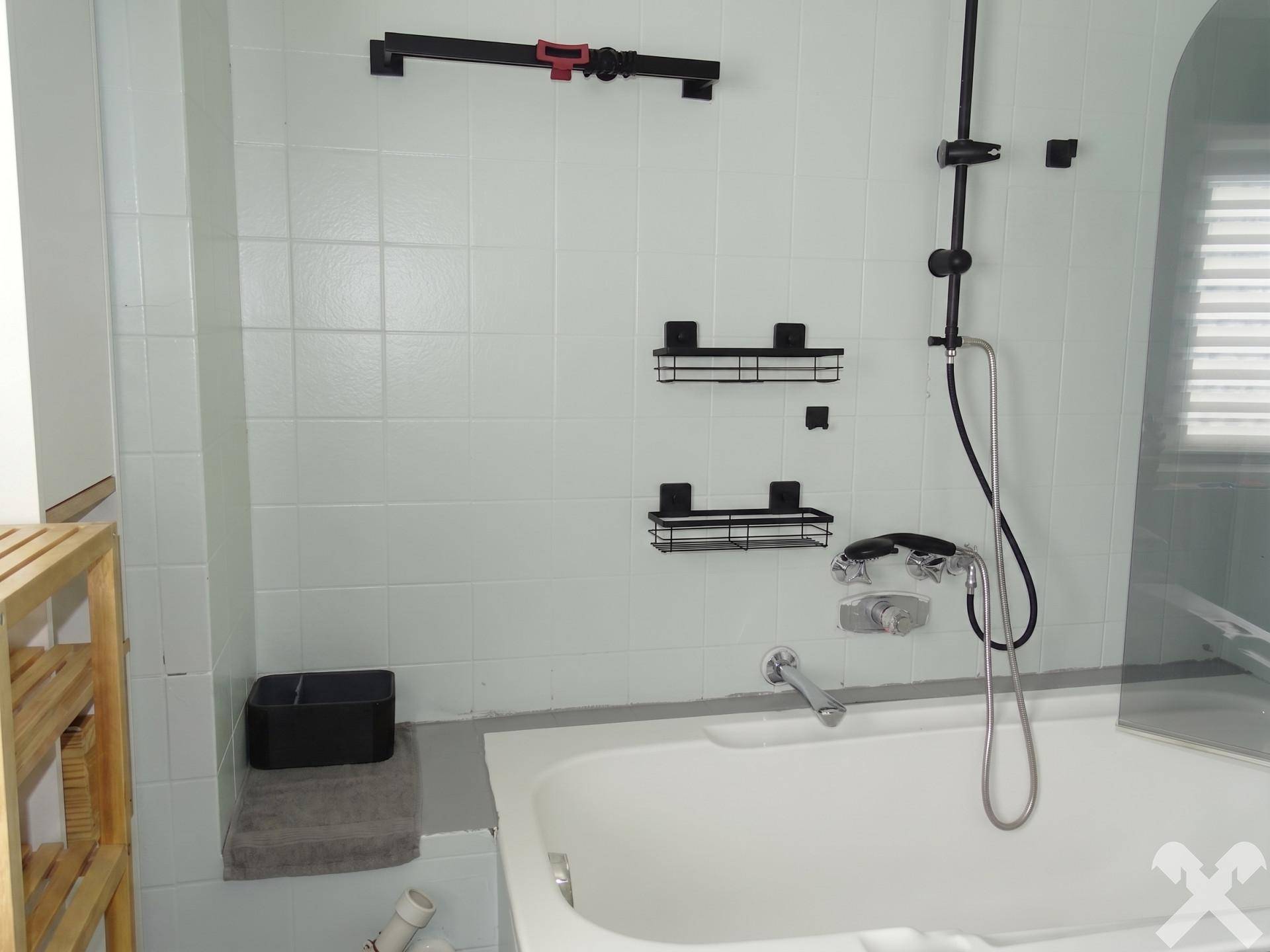 Badezimmer mit Badewanne und integrierter Duschfunktion, umgeben von hellen Fliesen.