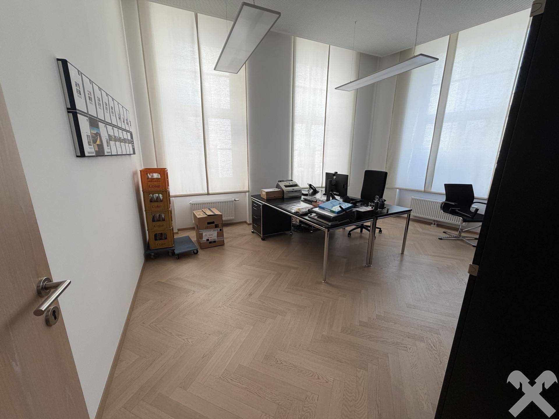 Helles Büro mit Fischgrätparkettboden, großen Fenstern und Schreibtisch.