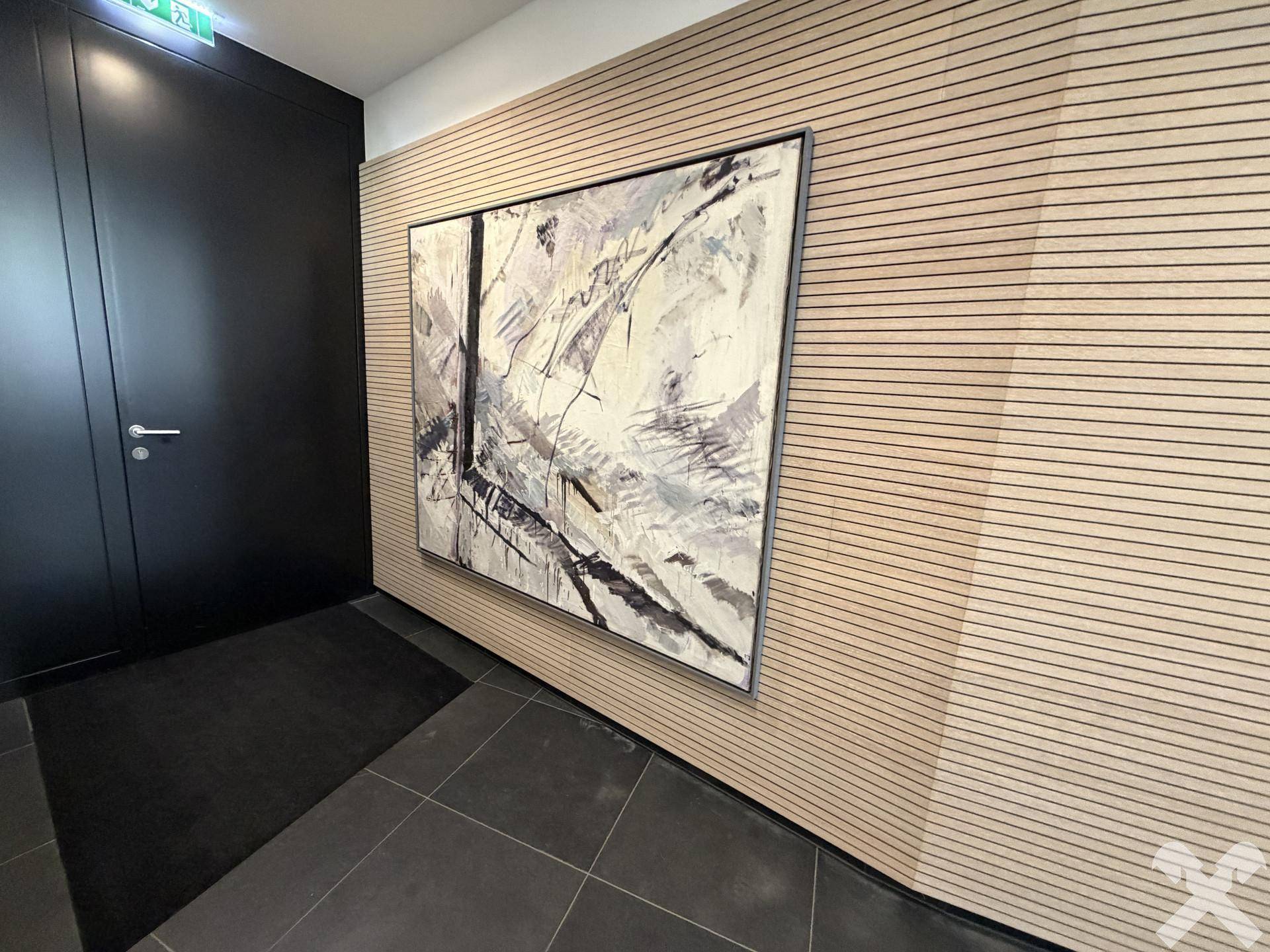 Moderner Eingangsbereich mit dunkler Tür, großem Kunstwerk und Holzlamellenwand.