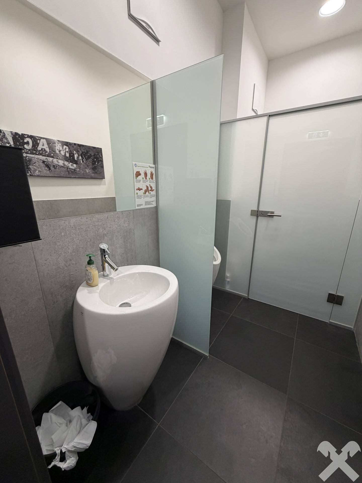 Modernes WC mit einzigartigem Waschbecken, Glasabtrennung und dunklen Fliesen.