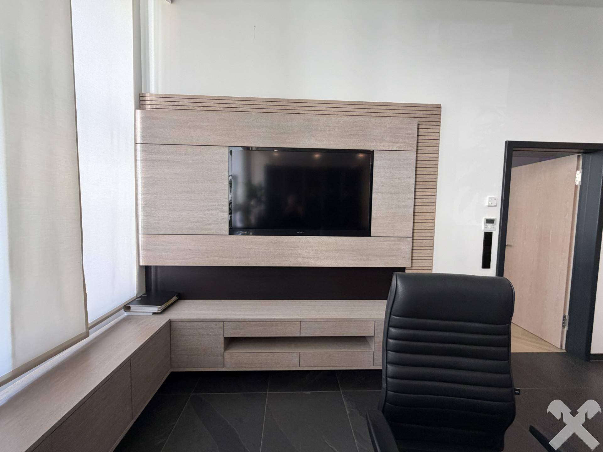 Büro mit großem Wandfernseher, integriertem Mediamöbel und Bürostuhl.