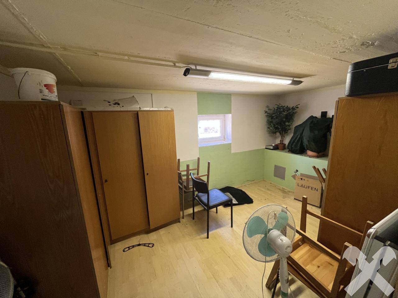 Kellerraum mit Holzschränken, einem Ventilator und einem kleinen Fenster, bietet zusätzlichen Stauraum.