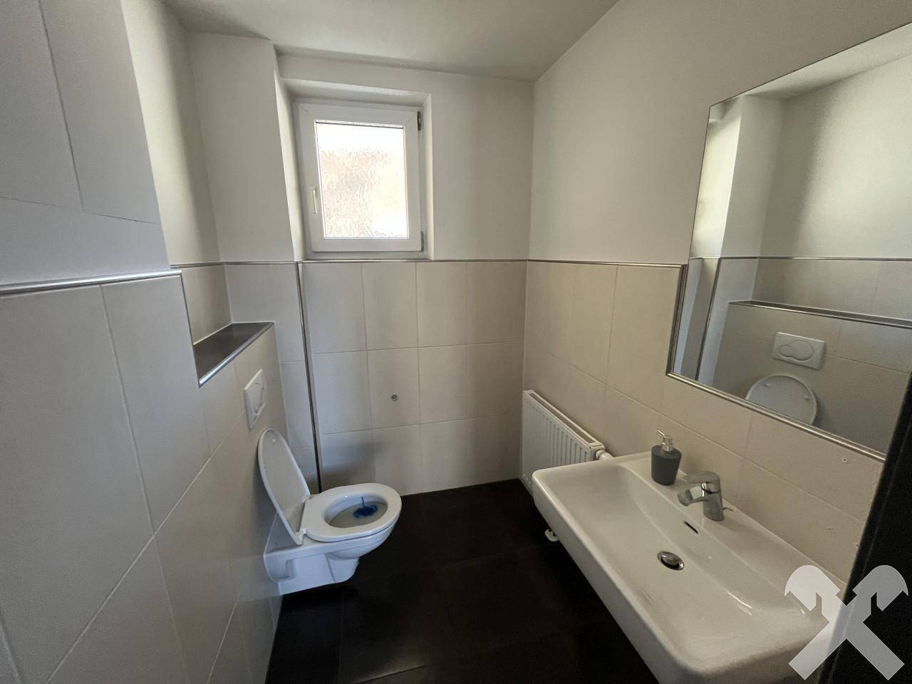 Modernes WC mit Wand-WC, Waschbecken und Fenster, hell gefliest.