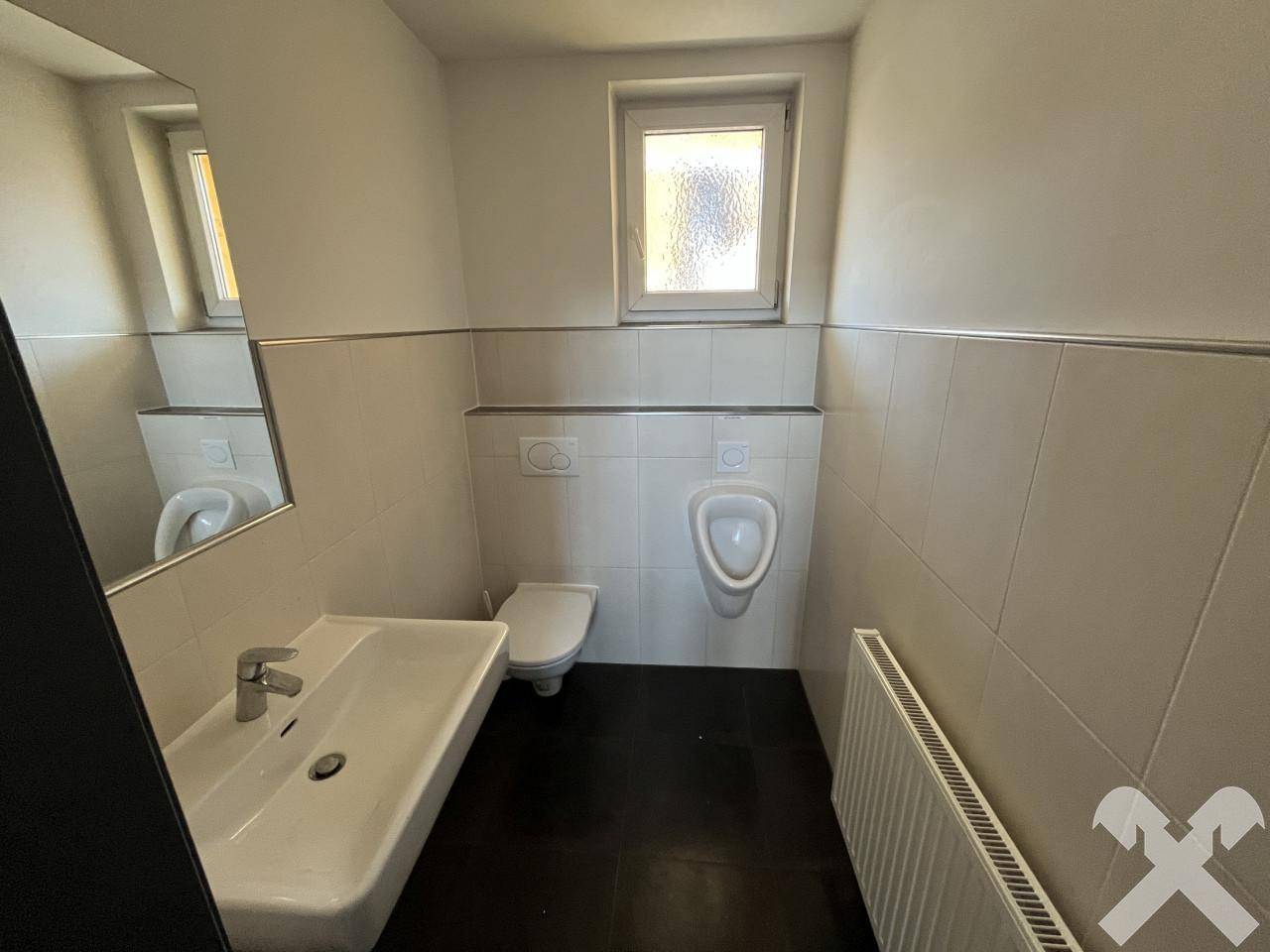 Modernes WC mit Urinal, Wand-WC, Waschbecken und Fenster, in hellen Fliesen.