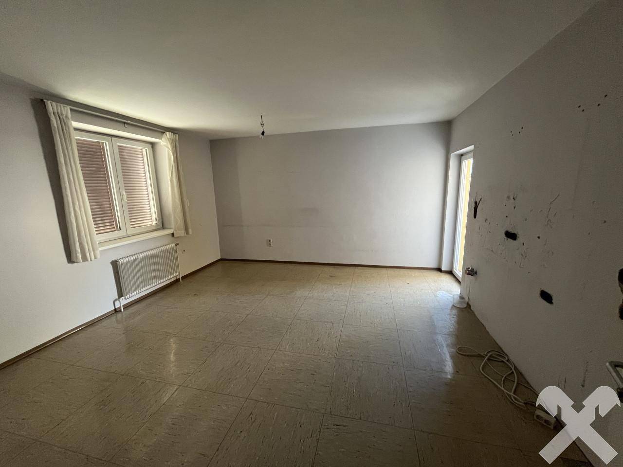 Leerer Raum mit Fliesenboden, Fenster und Heizkörper, bereit für die Einrichtung.