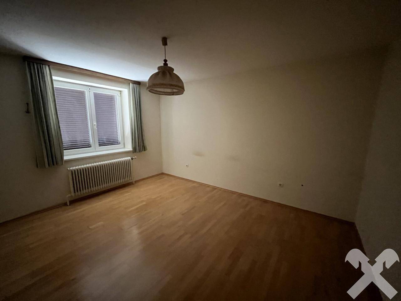Helles Schlafzimmer mit Parkettboden, Fenster und Deckenleuchte, in neutralen Farben.