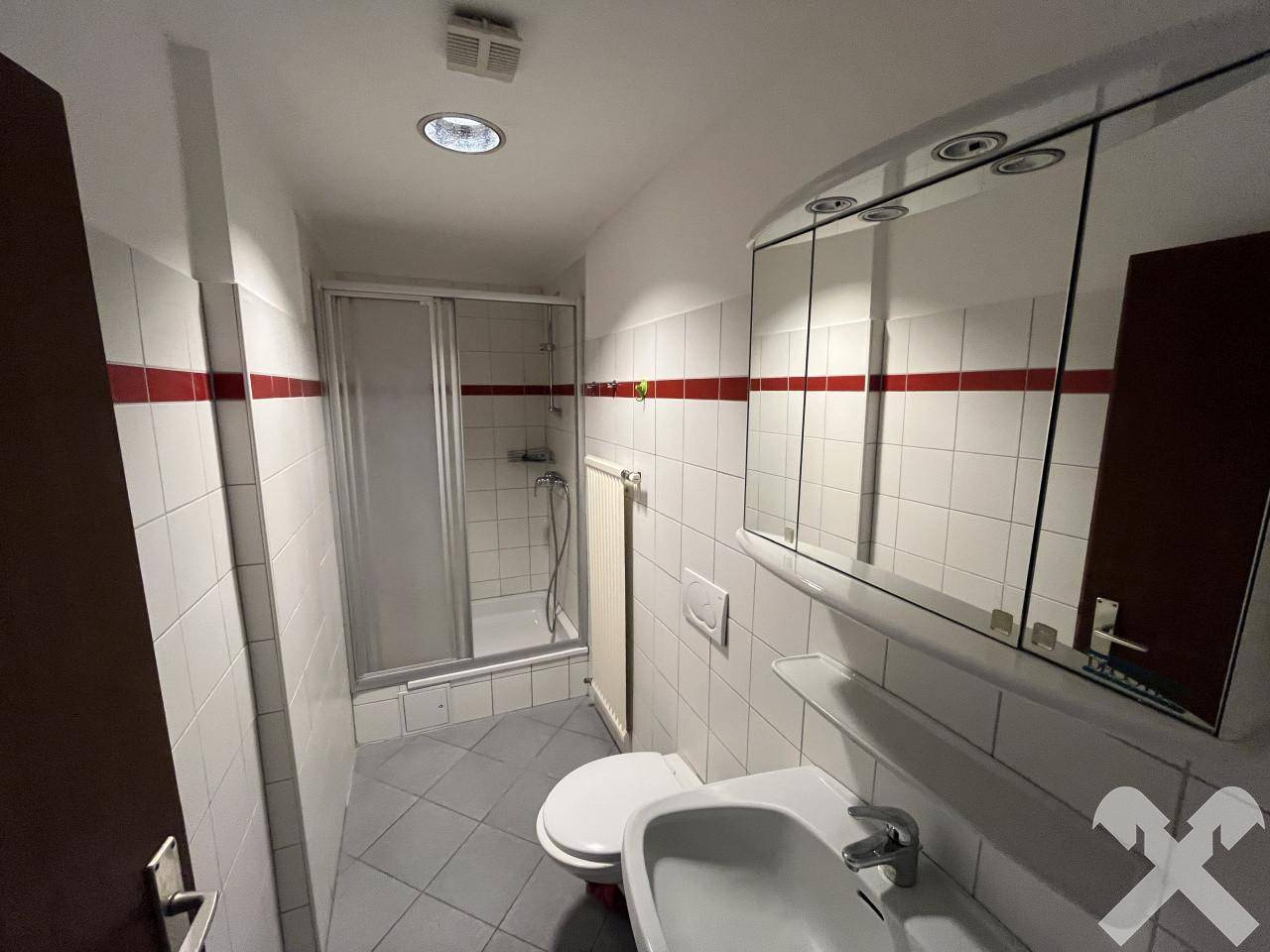 Badezimmer mit Dusche, WC, Waschbecken und Spiegelschrank, weiß gefliest.