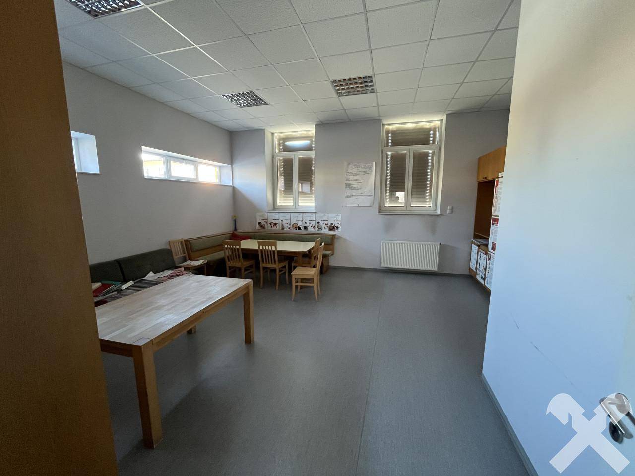Großer Gemeinschaftsraum mit Tischen, Bänken und Fenstern, hell und funktional.