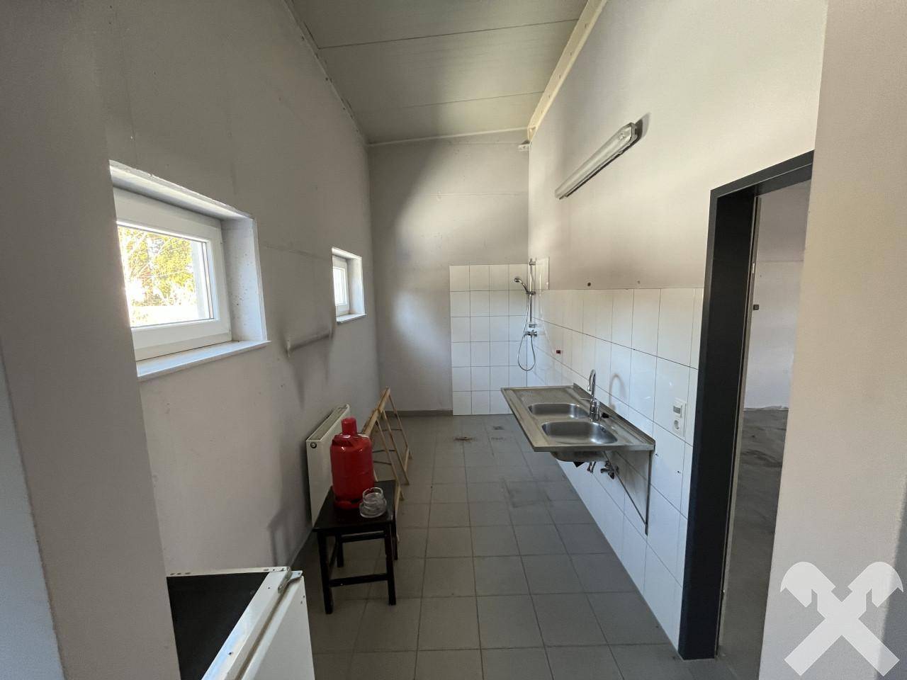 Einfacher Waschraum mit zwei Edelstahlwaschbecken, gefliesten Wänden und kleinen Fenstern für Belüftung.