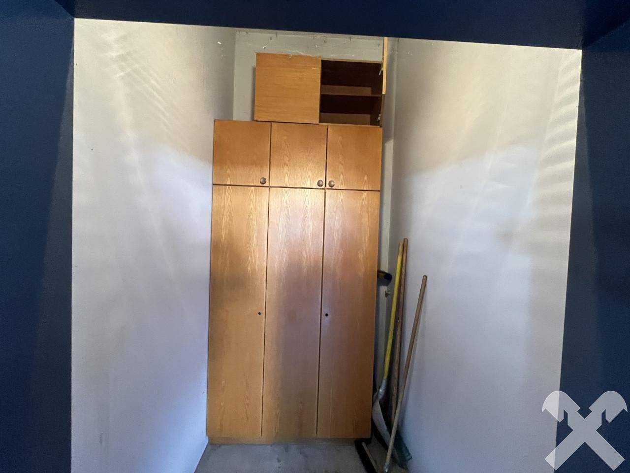 Schmaler Abstellraum mit einem hohen Holzschrank und Reinigungsgeräten, bietet praktischen Stauraum.